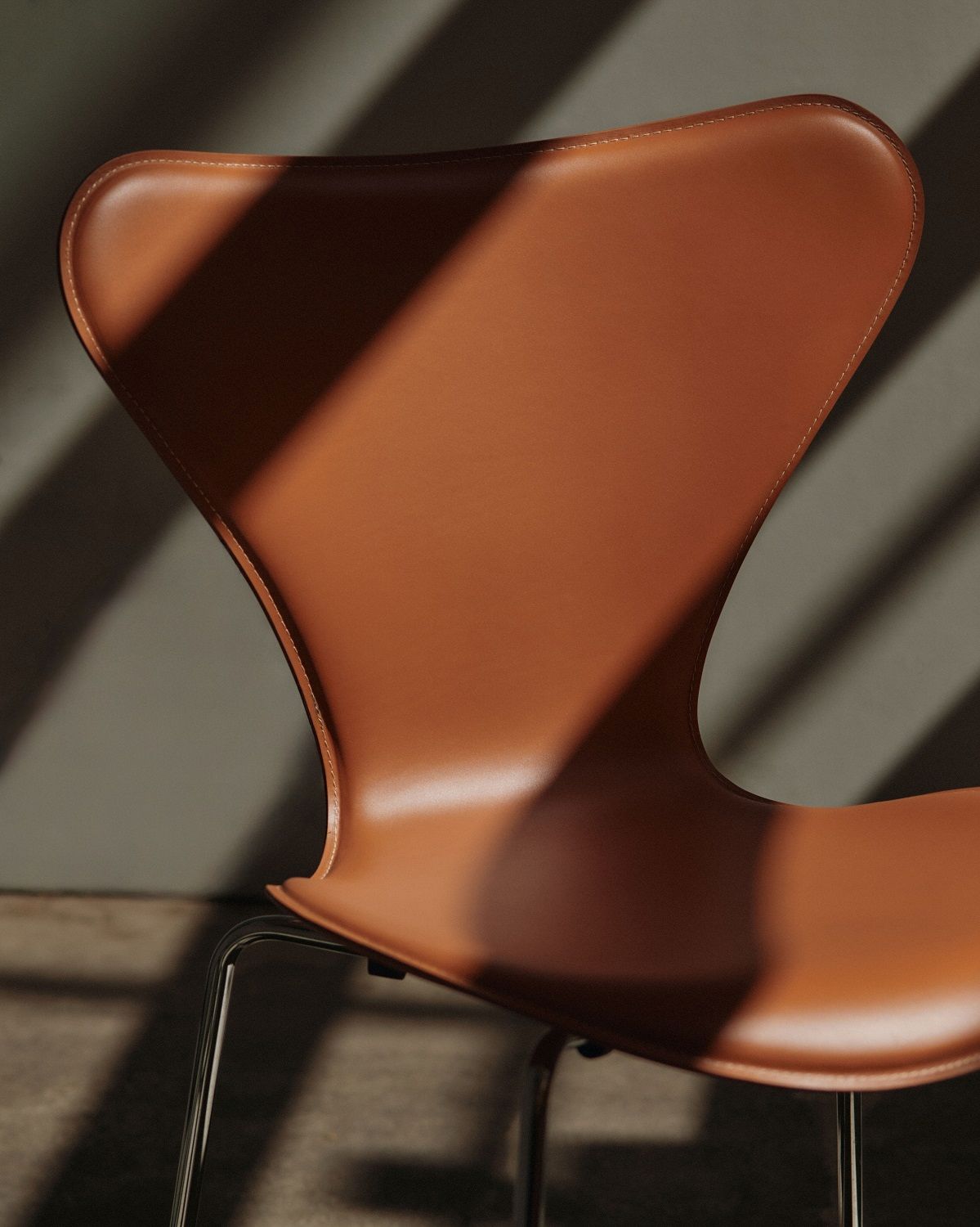 Detailaufnahme des Fritz Hansen Siebener Stuhls / Serie 3107 mit braunem Lederbezug und Chromgestell.