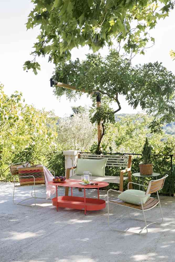 Somerset Bank von Fermob im Garten, mit Outdoor-Möbeln und rotem Tisch.