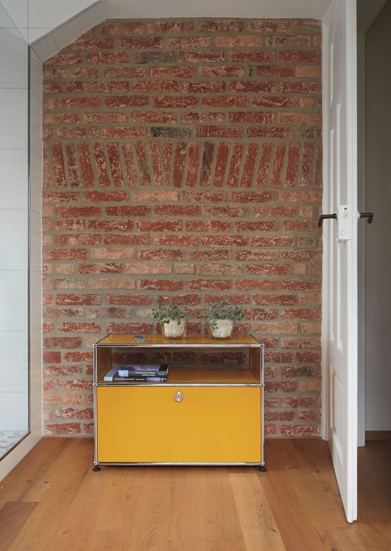 Gelbes USM Haller Beistellmöbel mit einer Klappe vor einer Backsteinwand und Holzboden.