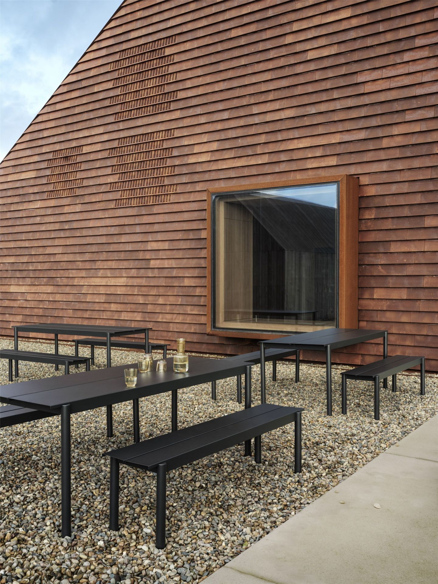 Muuto Linear Steel Outdoor Tisch 200x75 cm, schwarzer Gartentisch mit Bänken auf Kies.