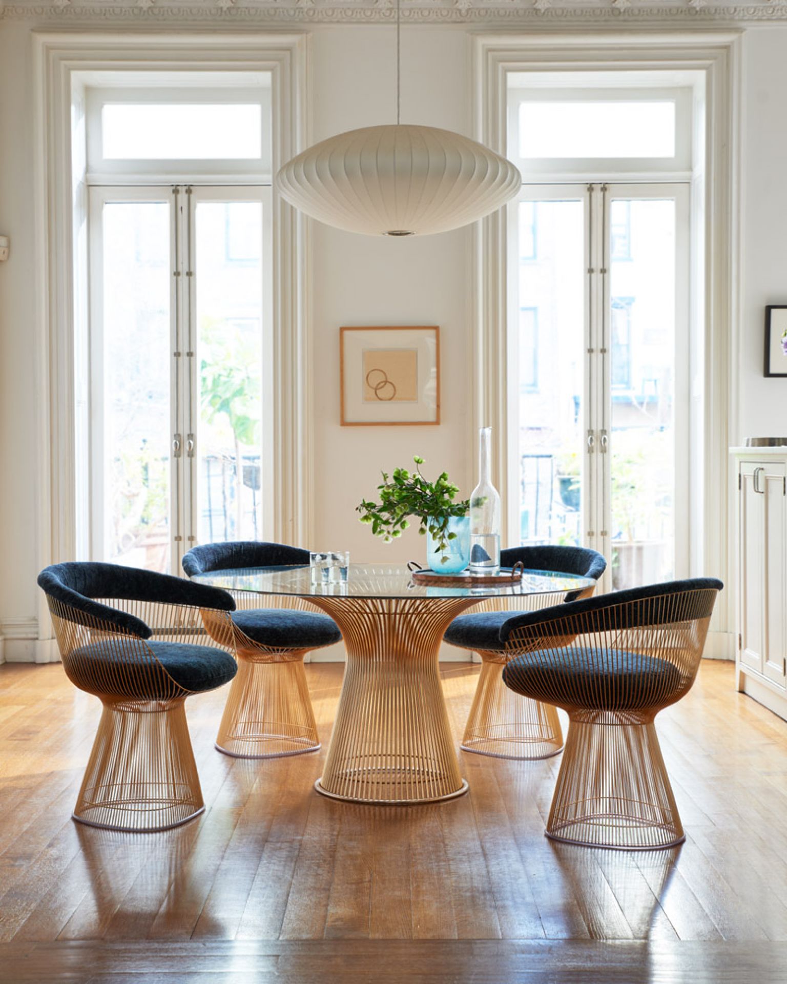 Esszimmer mit Platner Tisch von Knoll International, Glasplatte und goldenem Drahtgestell, umgeben von Stühlen.