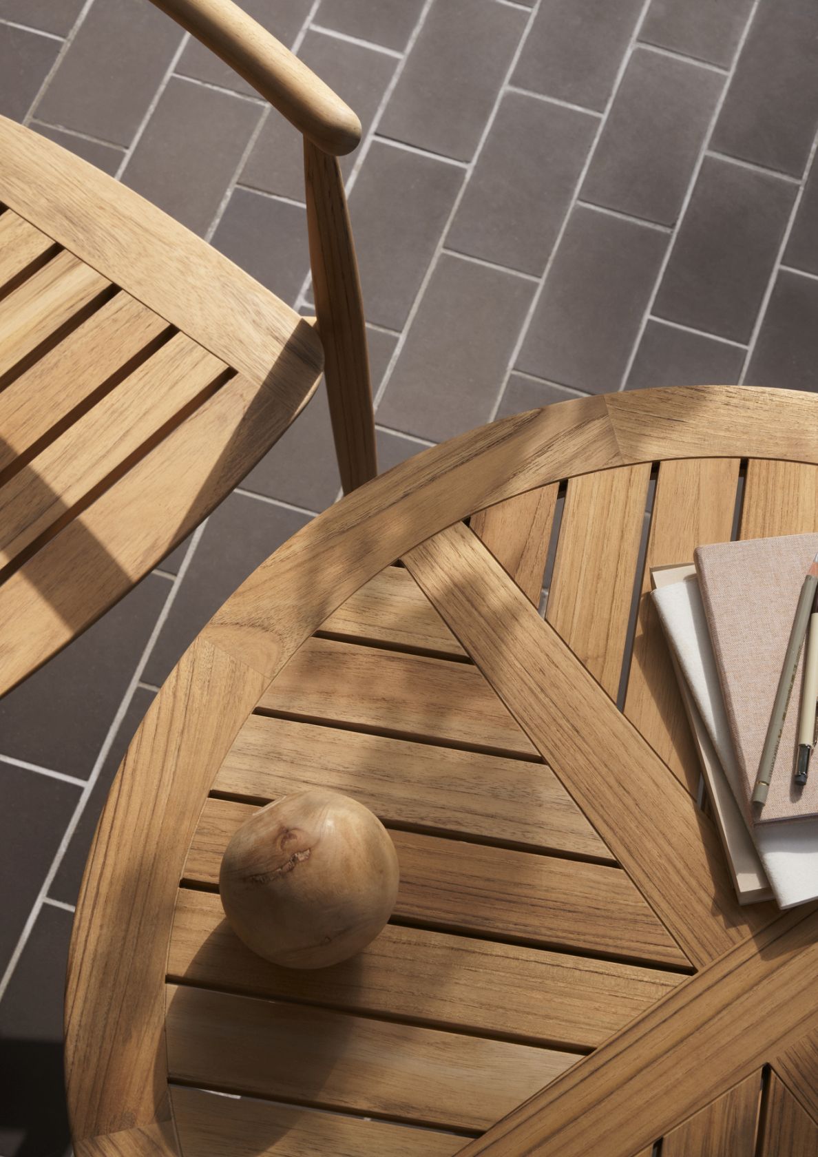 Detailaufnahme des Carl Hansen E022 Embrace Outdoor Tisches aus Teakholz mit Notizbüchern und Holzobjekt.