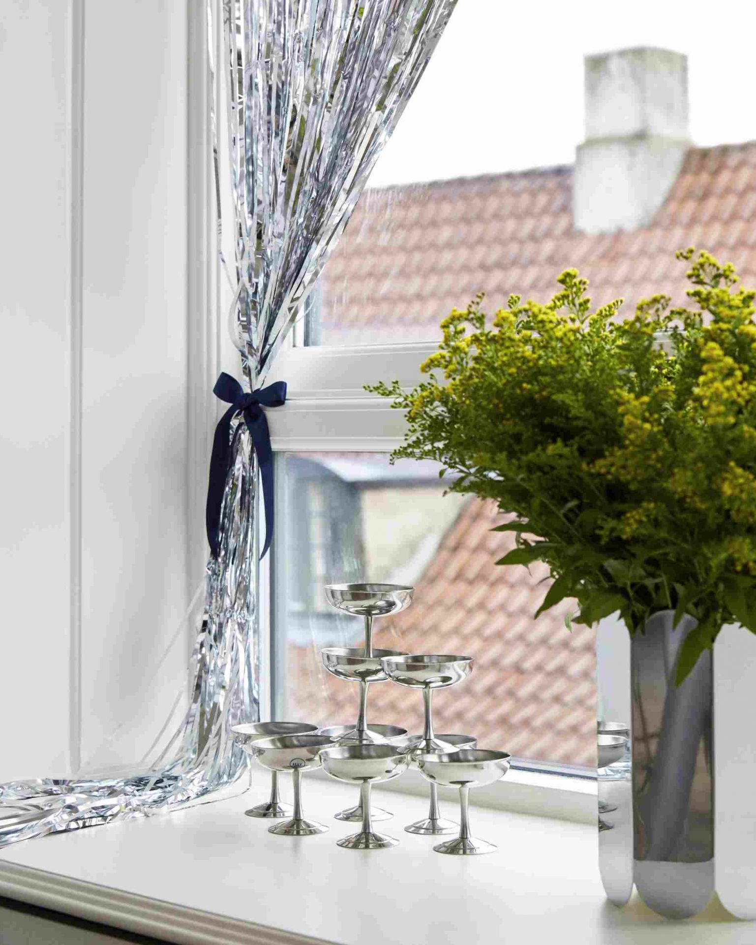Hay Arcs Vase L Mirror neben Champagnergläsern und silberner Lametta-Deko am Fenster, festliche Tischdekoration.