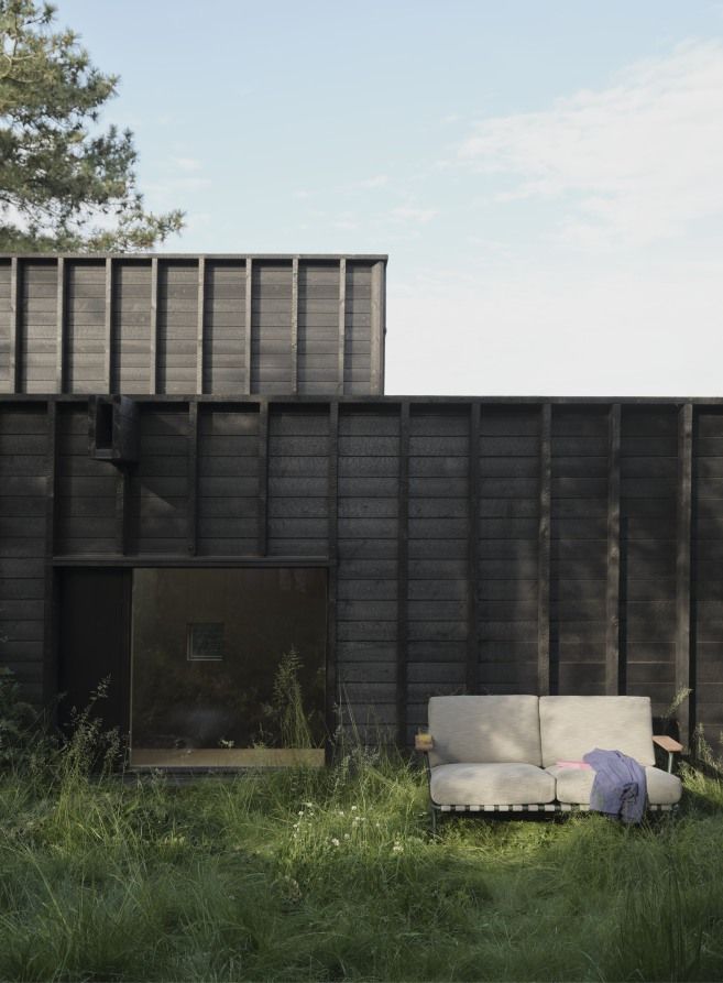 Muuto Settle Outdoor Sofa 2-Sitzer in Beige vor einem modernen Holzhaus im Grünen.