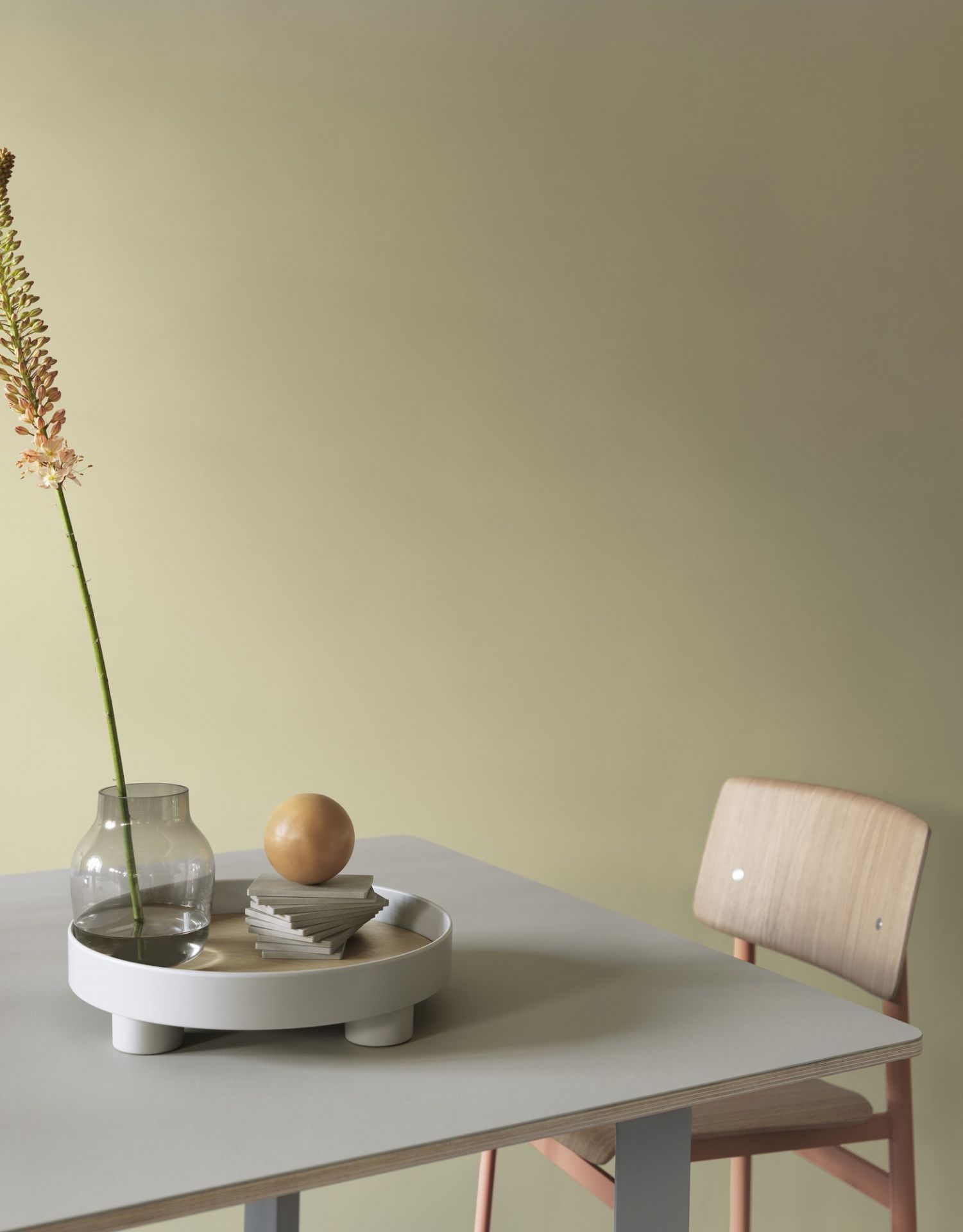 Muuto Loft Chair Stuhl aus Holz neben Esstisch mit Dekoration und Vase vor olivgrüner Wand.