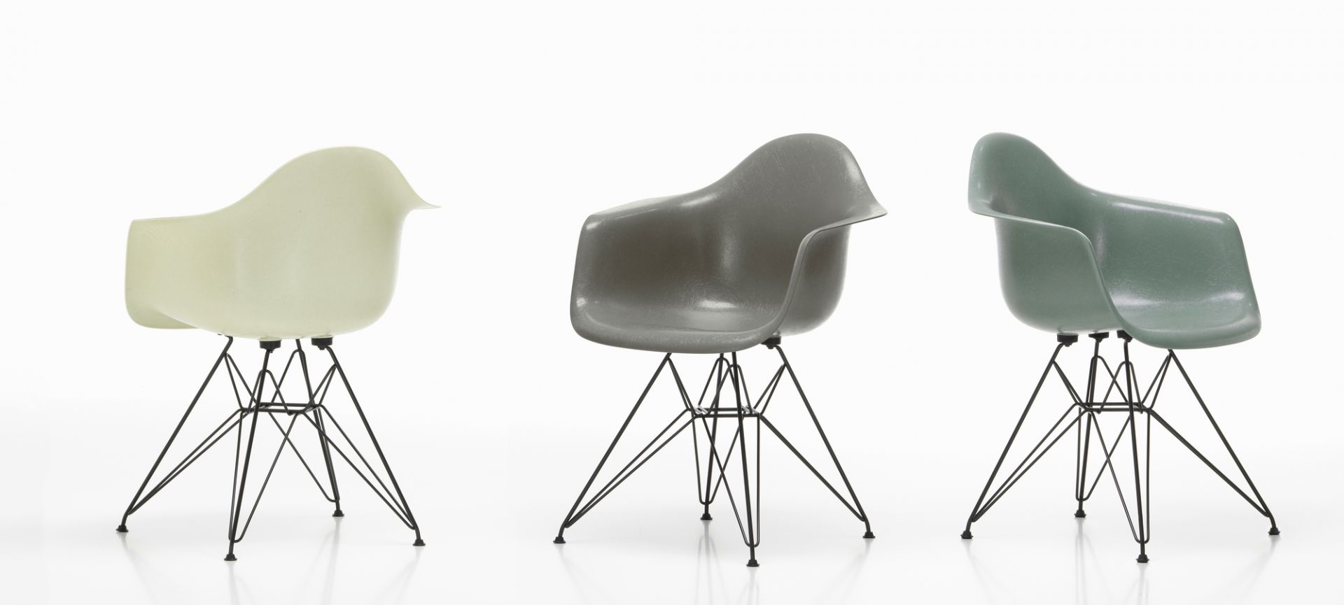 Drei Vitra Eames Fiberglass Arm Chairs DAR Stühle in Weiß, Grau und Grün auf filigranem Metallgestell.