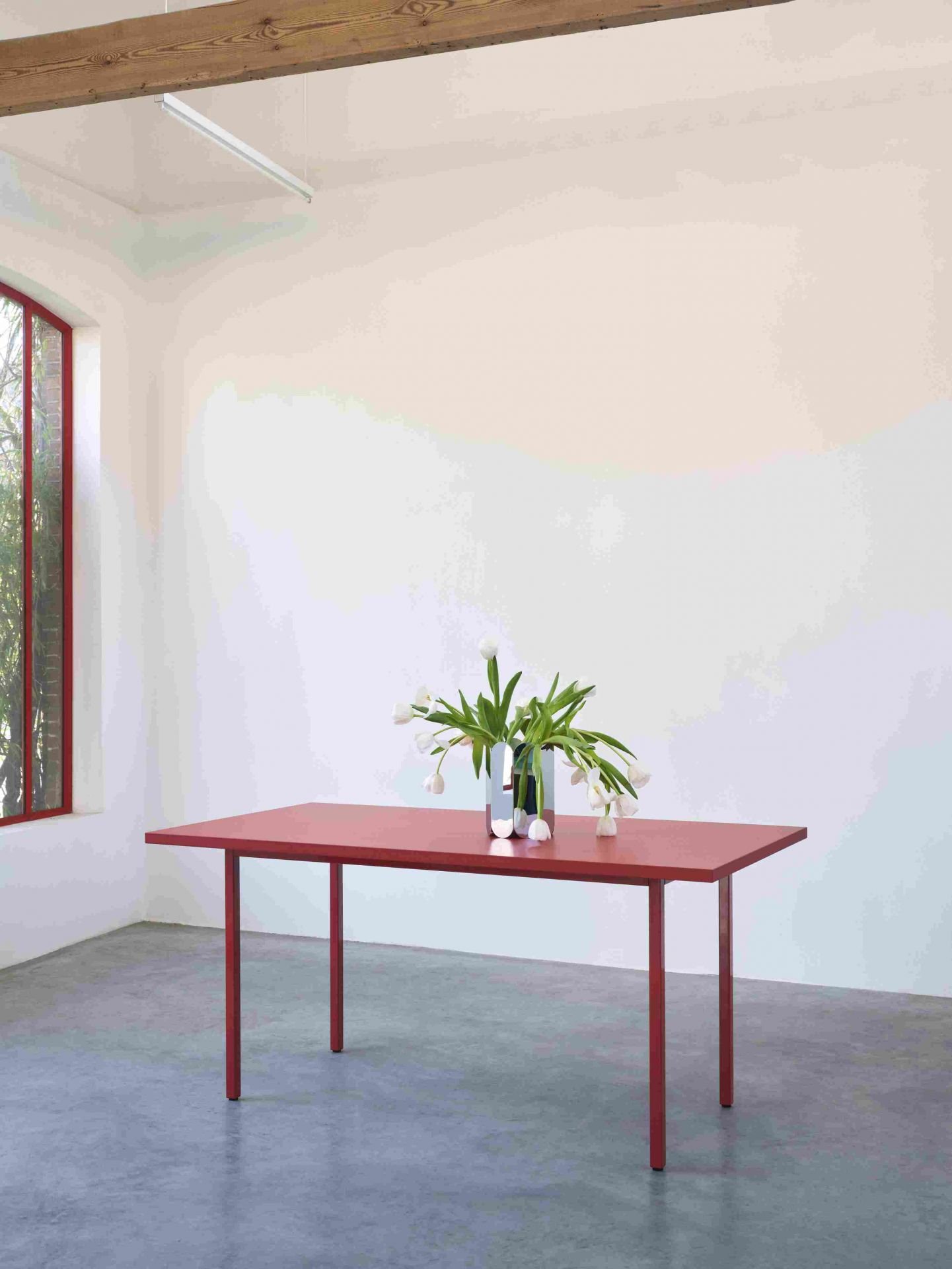 Hay Arcs Vase L Mirror auf rotem Tisch mit weißen Tulpen in minimalistischem Raum.