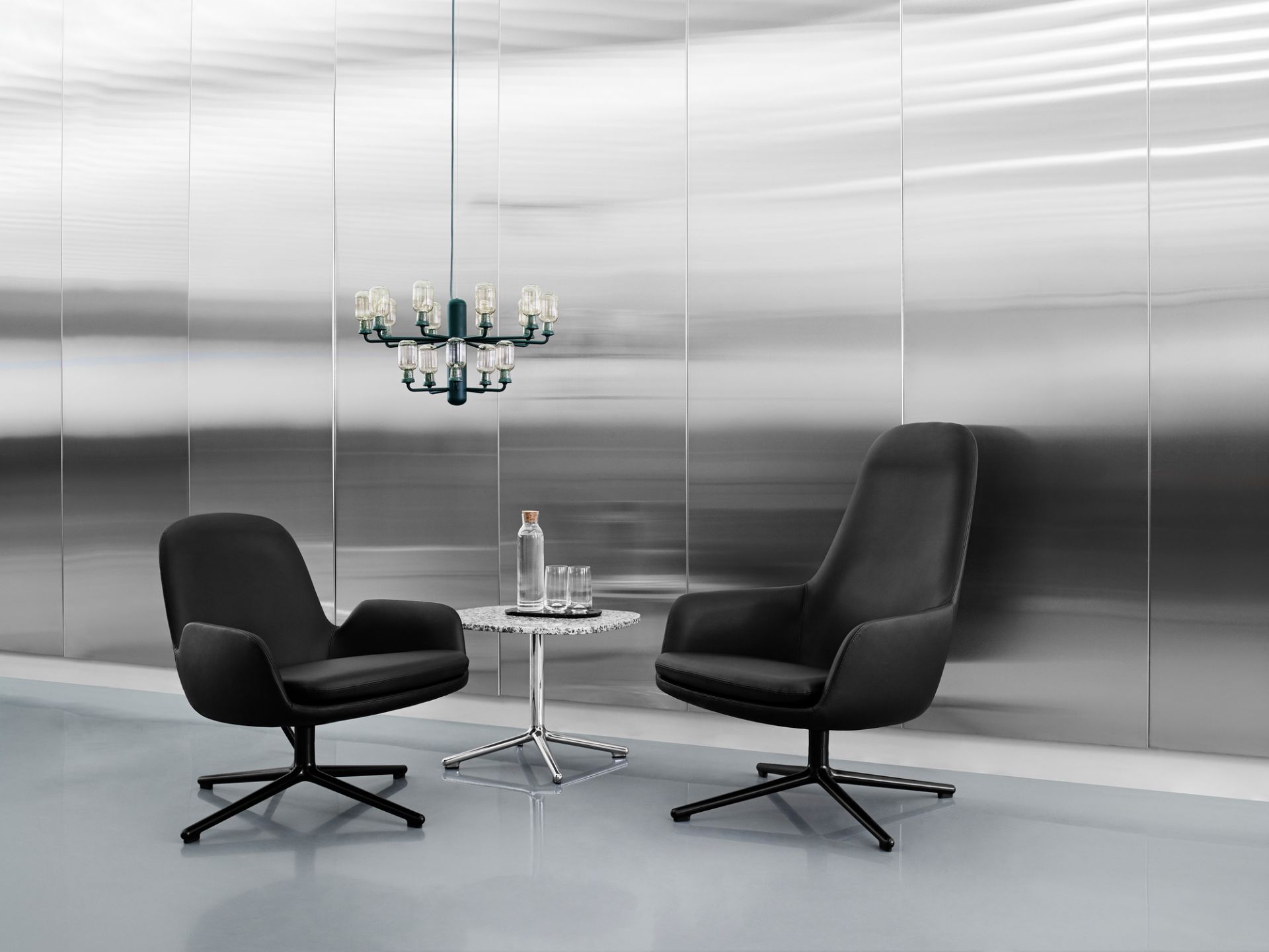 Normann Copenhagen Amp Chandelier Pendelleuchte über schwarzem Sessel-Set mit Marmortisch in modernem Interieur.