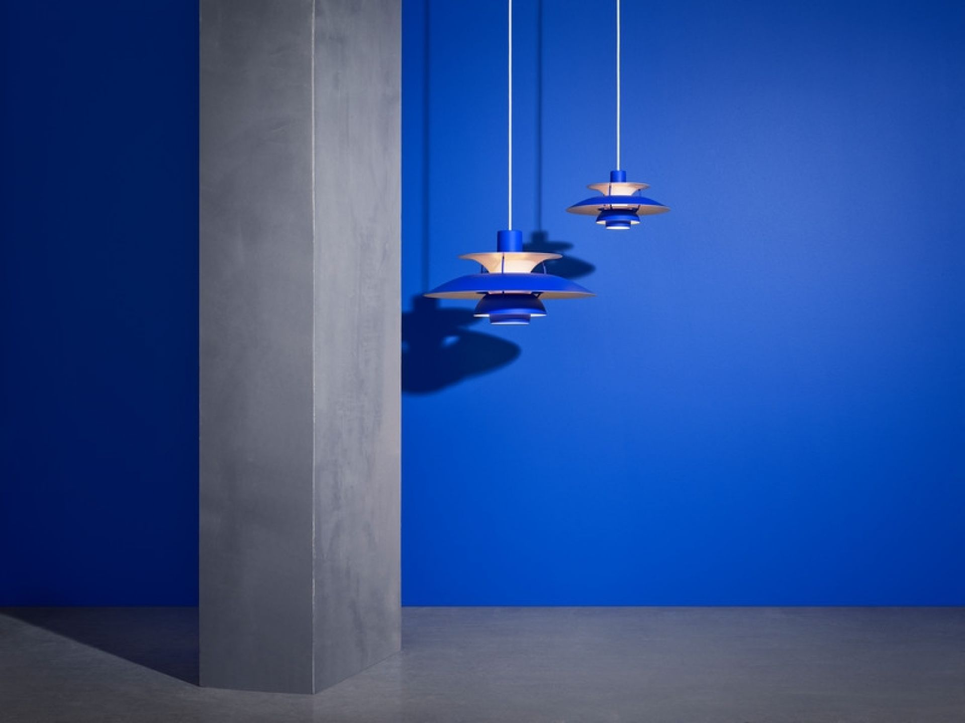 Zwei blaue PH 5 Mini Pendelleuchten von Louis Poulsen vor blauem Hintergrund. Designleuchte.