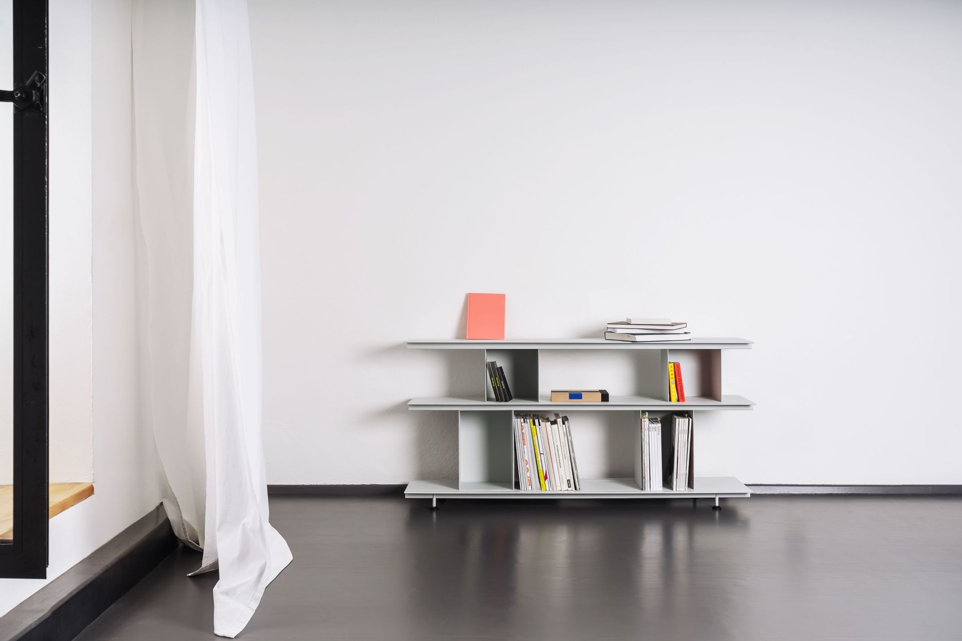Helles Zimmer mit Zoll D Regal von Nils Holger Moormann, gefüllt mit Büchern und Zeitschriften.
