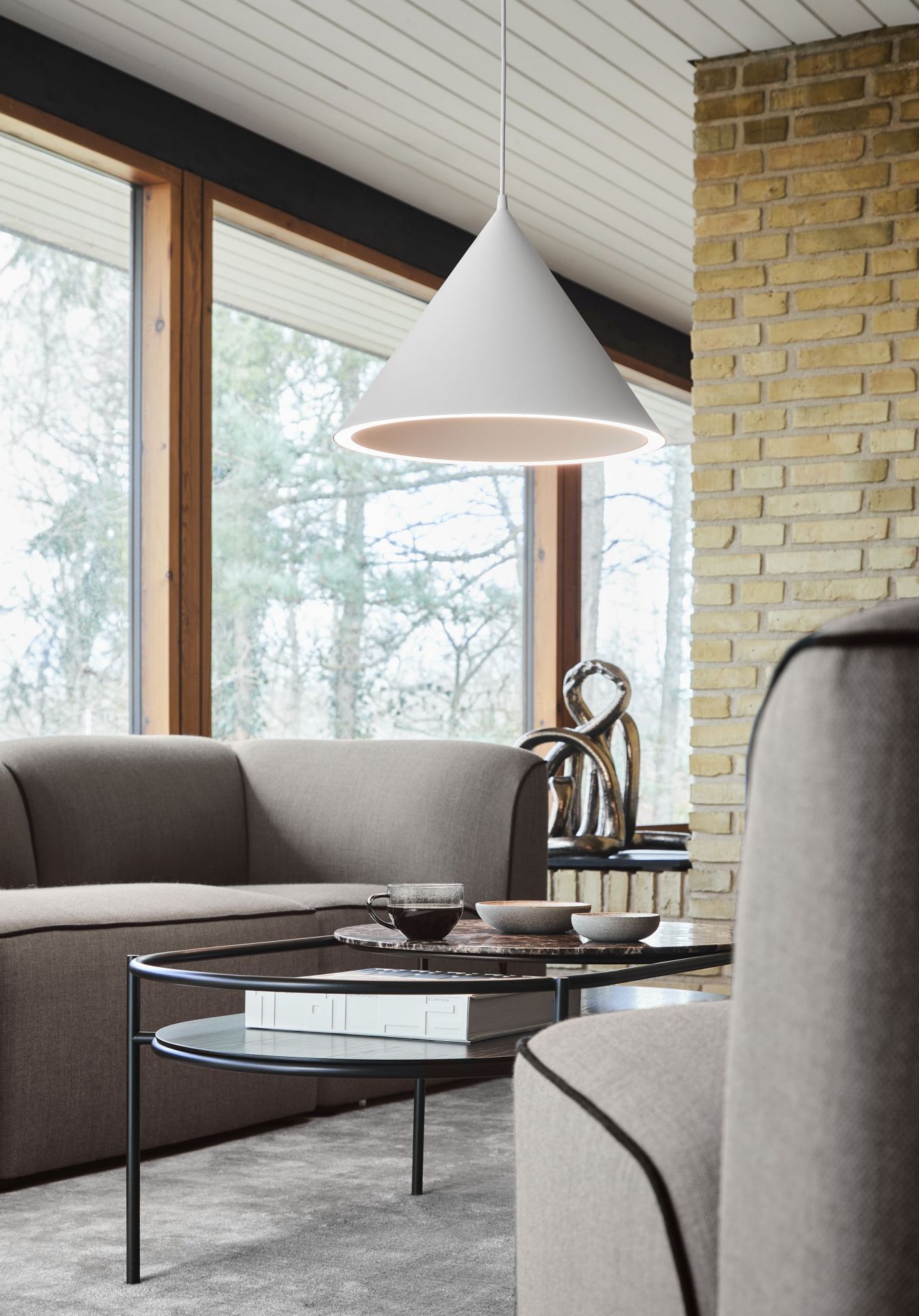 Nahaufnahme der weißen Annular Pendelleuchte von Woud über einem stilvollen Wohnzimmer mit Designermöbeln.
