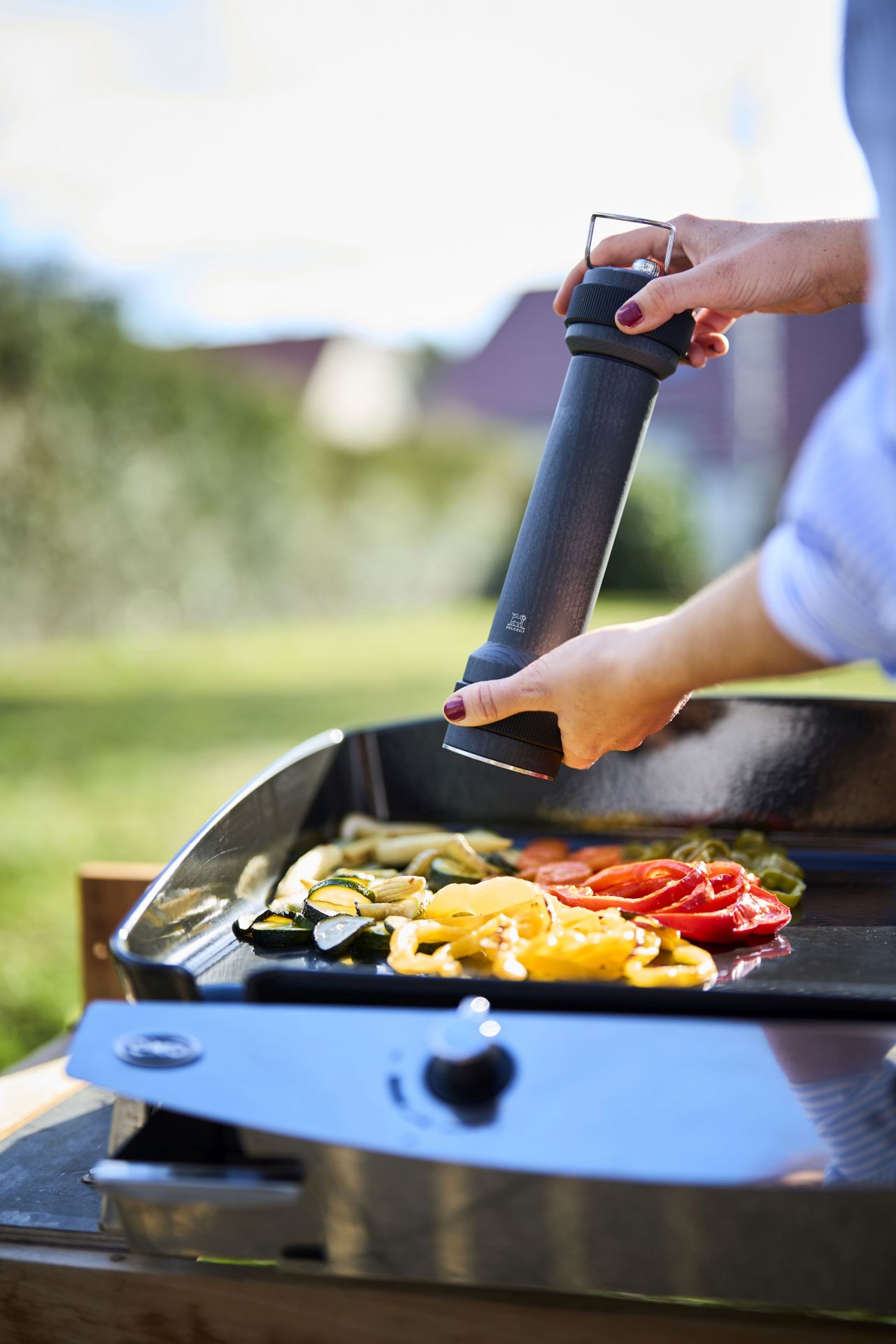 Frau würzt Gemüse auf Grill mit Peugeot BBQ Pfeffermühle Graphit 30 cm im Freien.