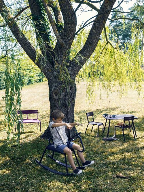 Junge auf Adada Schaukelpferd von Fermob im Garten unter Baum. Outdoor Spielzeug für Kinder.