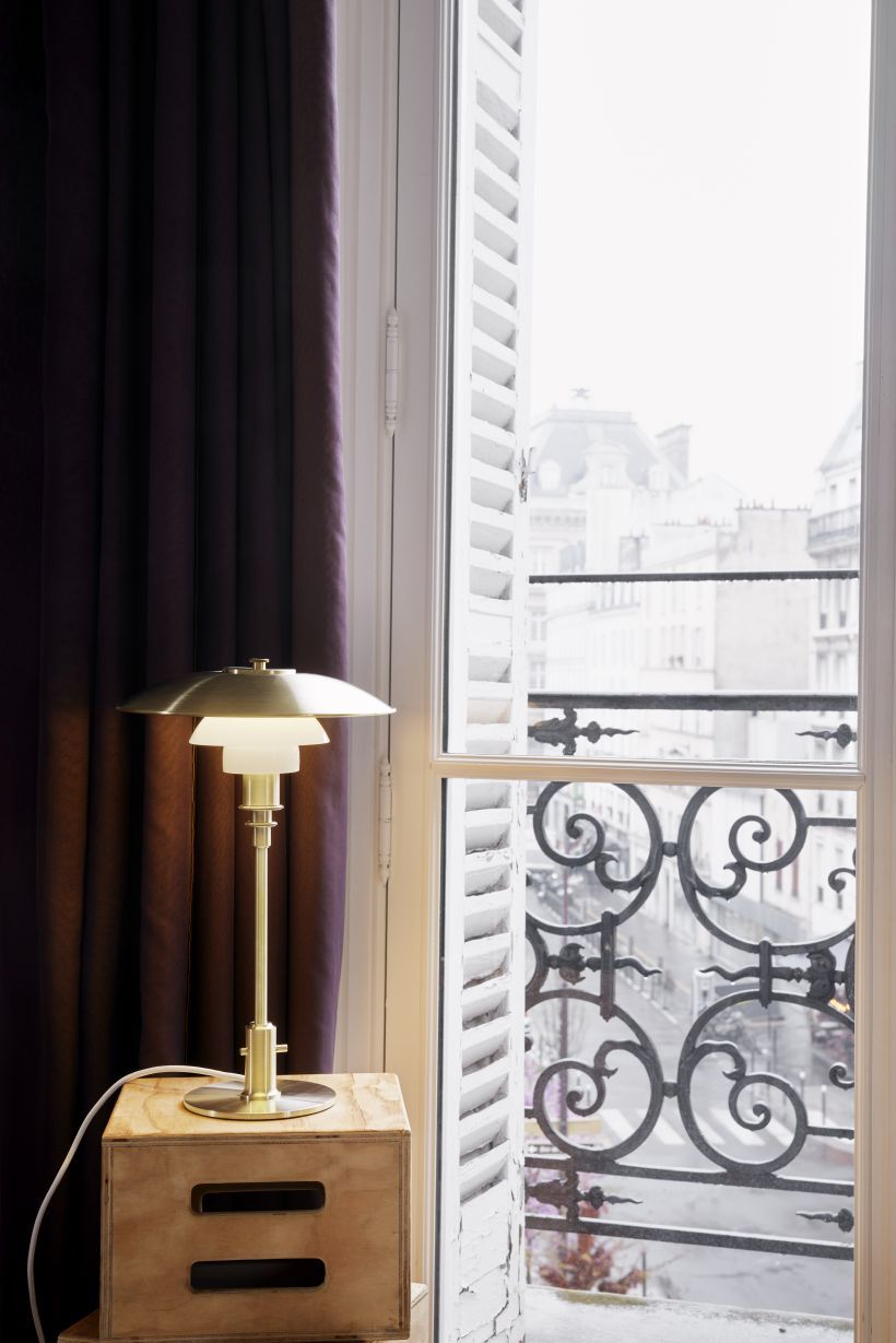 PH 3/2 Tischleuchte Messing von Louis Poulsen neben einem Fenster mit Stadtblick.