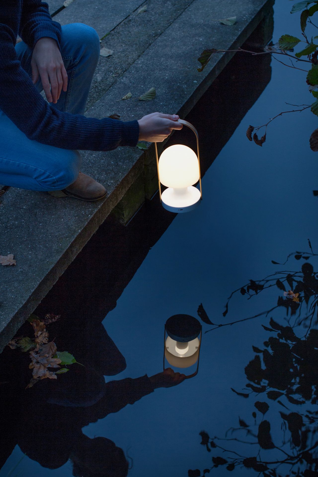 FollowMe LED Akkuleuchte von Marset: Tragbare Tischleuchte mit warmem Lichtschein am Wasser.