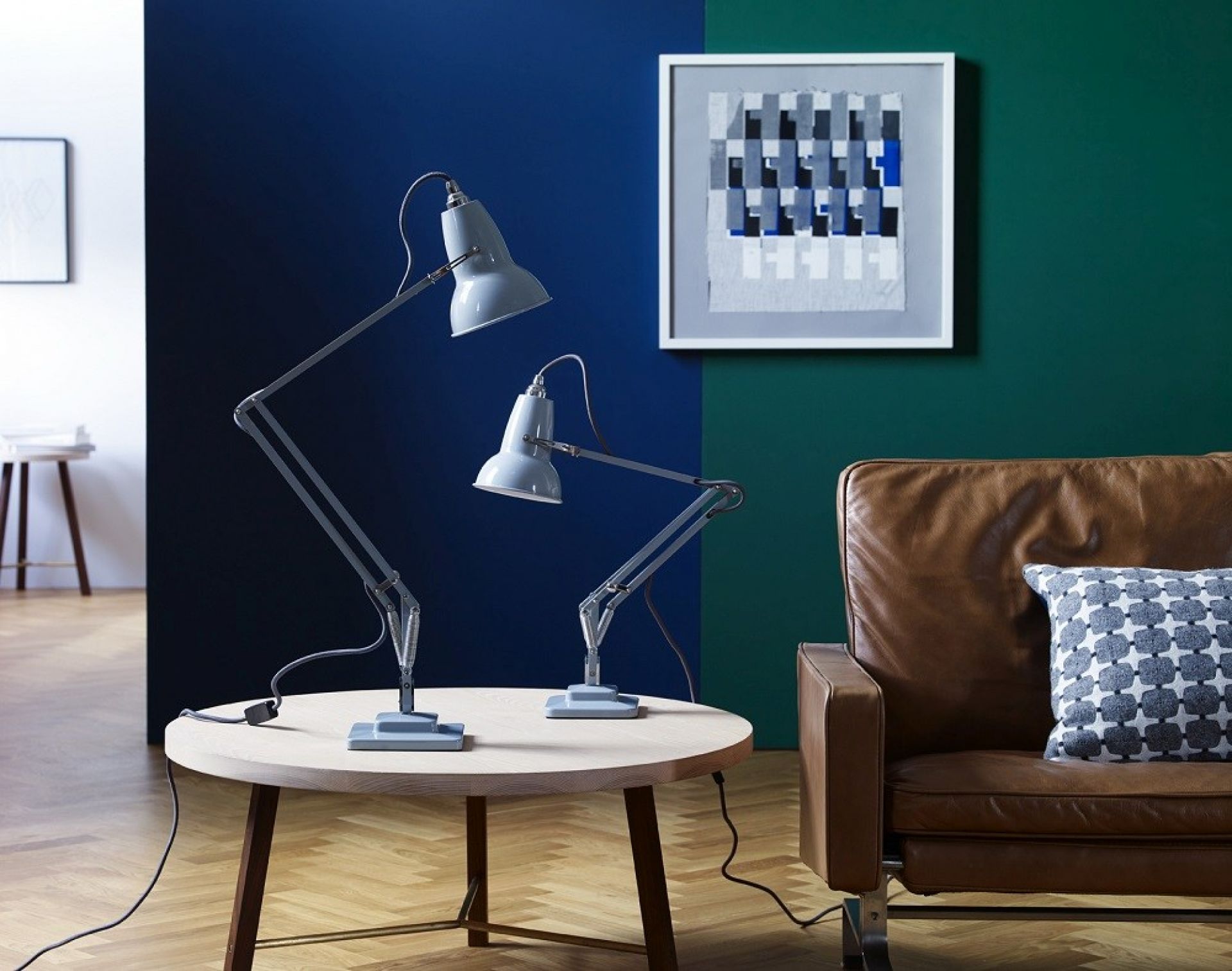Zwei graue Anglepoise Original 1227 Mini Tischleuchten auf einem Holztisch in einem Wohnzimmer.
