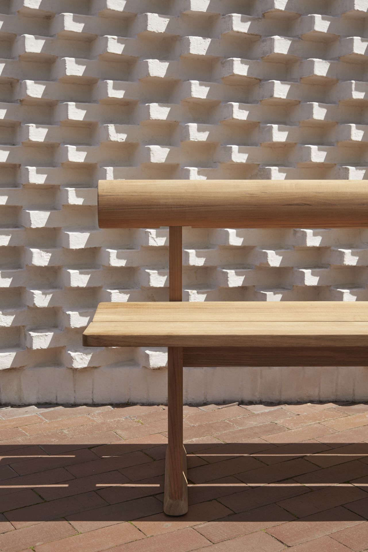 Banco Bank Teak Outdoor Bank von Skagerak by Fritz Hansen vor weißer Ziegelwand.