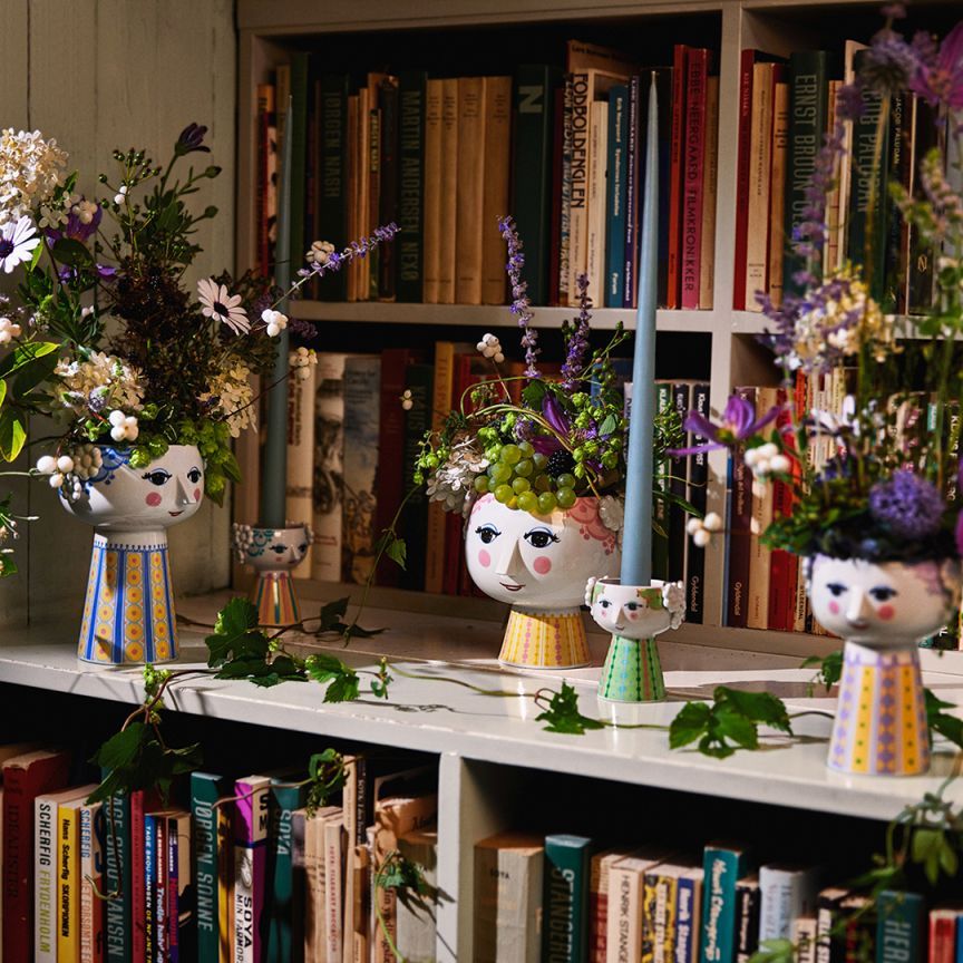 Drei hellblaue Bjørn Wiinblad Eva Vasen mit Blumen und Kerzenhaltern vor einem Bücherregal.