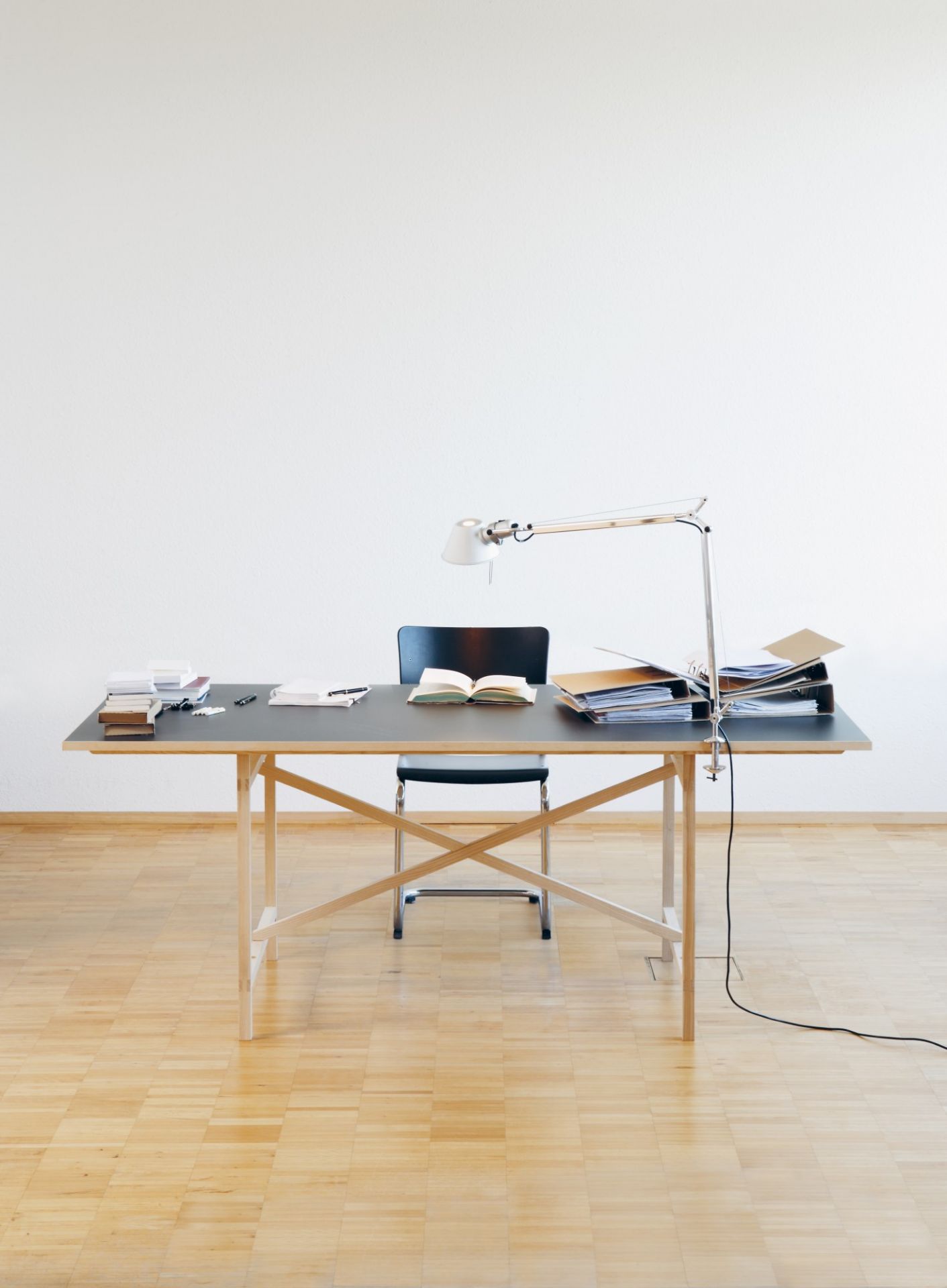 Egon Tisch von Nils Holger Moormann mit Lampe, Büchern, Ordnern und Stuhl auf Parkett.