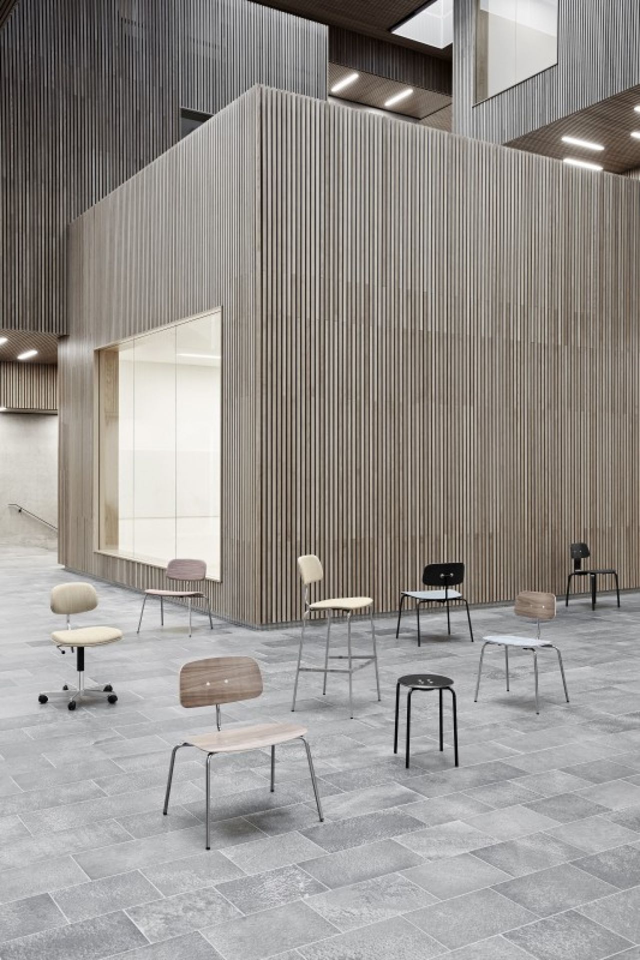 Kevi Stuhl Kollektion: Bürostuhl, Barhocker und Holzstühle in verschiedenen Ausführungen vor einer Holzwand.