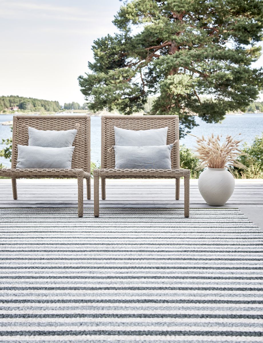 Pappelina Teo Teppich 230x320 cm mit grau-weißen Streifen auf einer Terrasse mit zwei Stühlen.