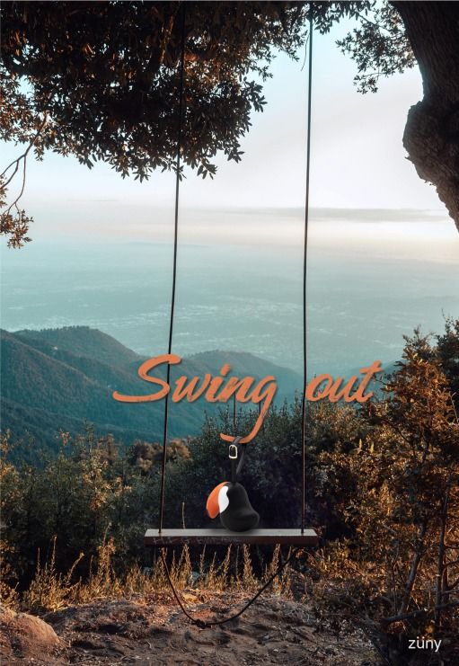 Bag Charm Taschenanhänger Tukan Toco Schwarz/Orange auf einer Schaukel mit Bergpanorama im Hintergrund.