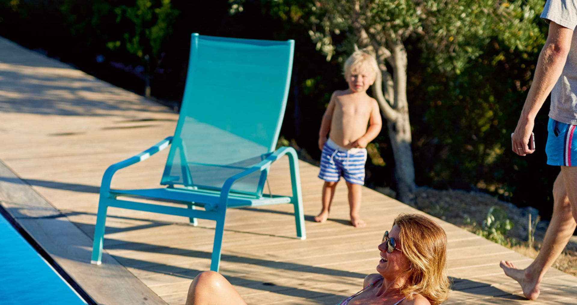 Türkisfarbener Alizé Sessel von Fermob am Pool, Familie genießt den Sommer auf der Holzterrasse.