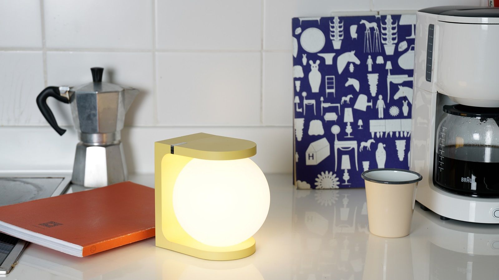 Gelbe Plat Reading Lamp Tischleuchte von house of home auf einer Küchentheke, neben Kaffeekanne.