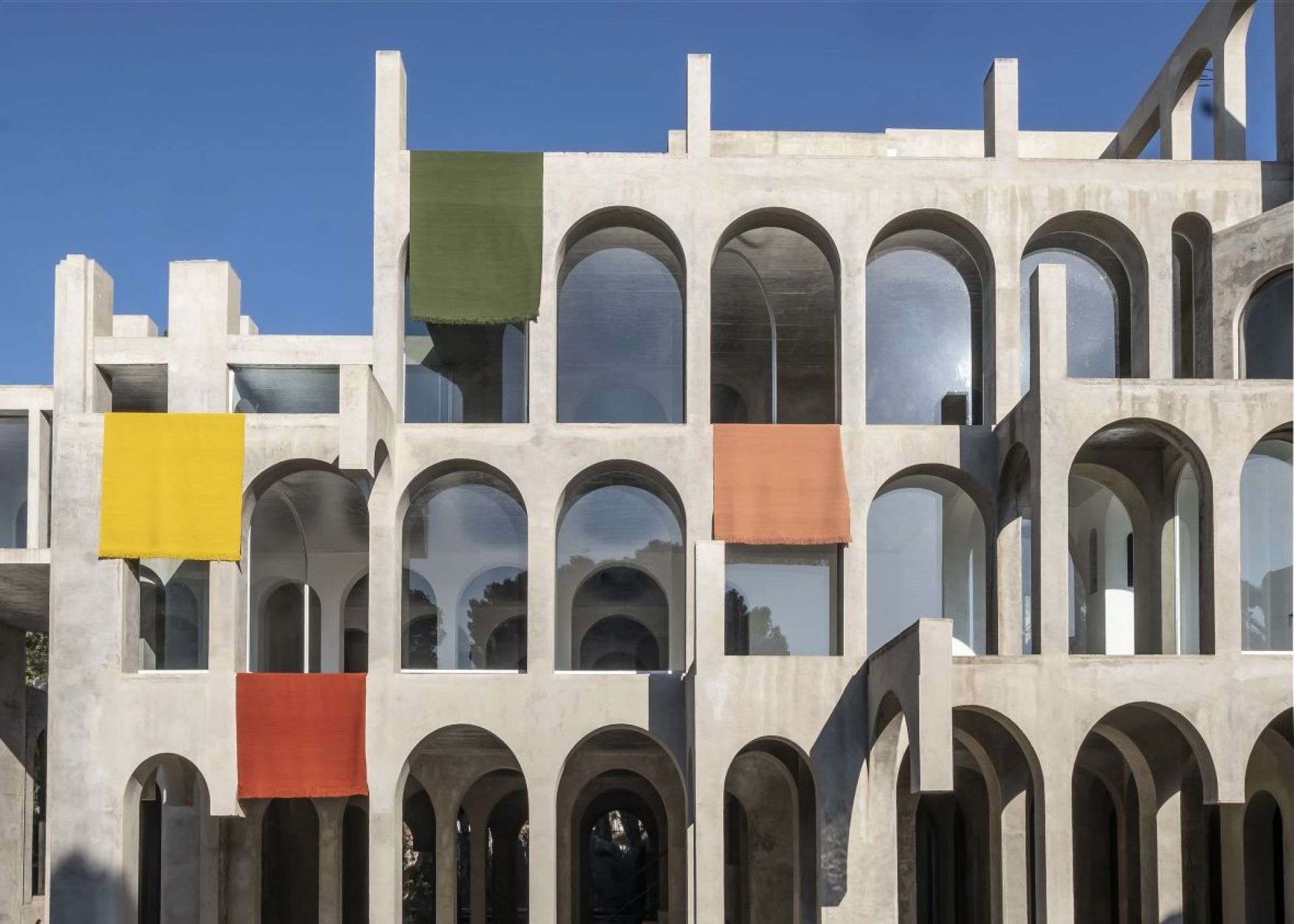 Architektonisches Gebäude mit farbigen Teppichen, die an den Fenstern hängen, darunter ein gelber, grüner und oranger Teppich.