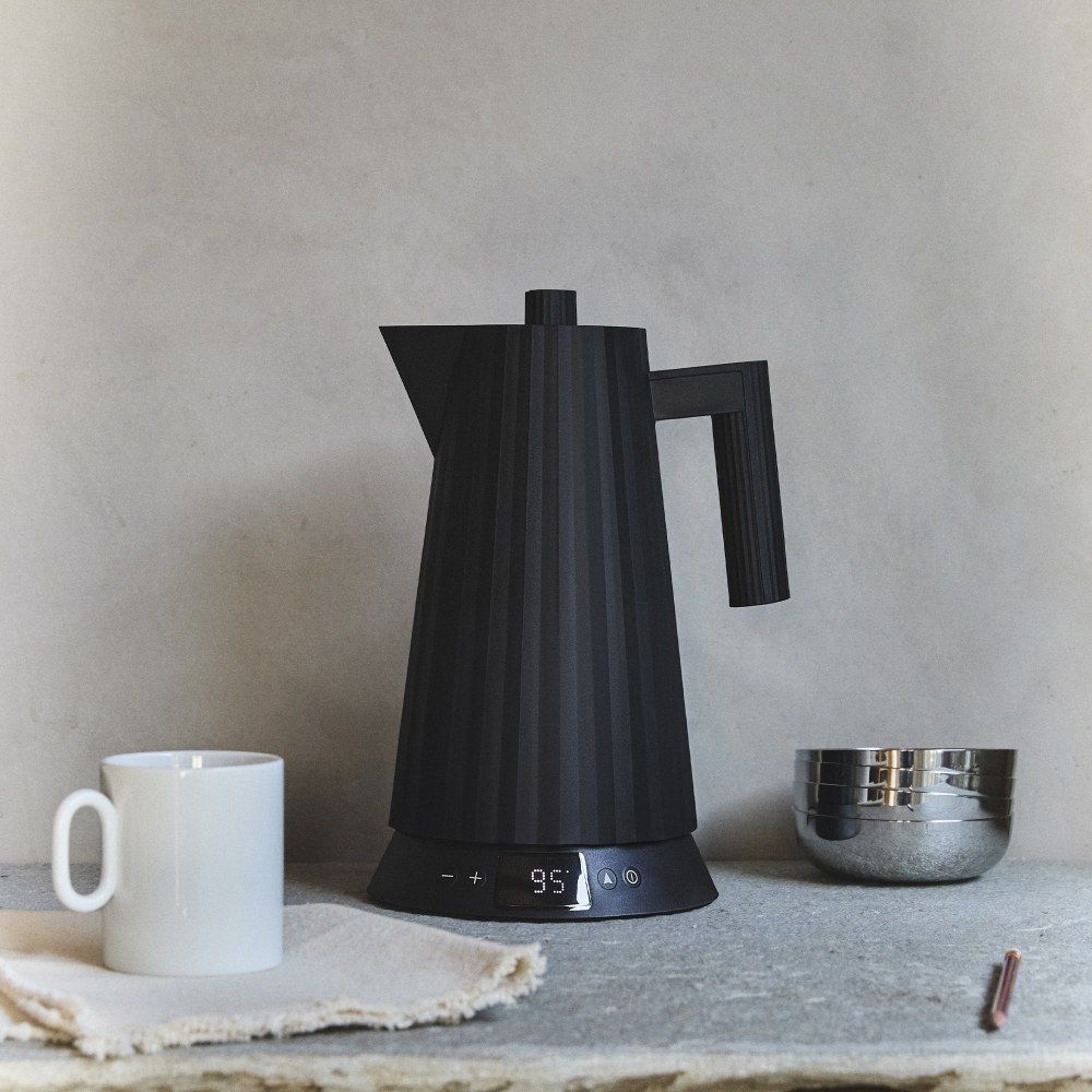 Schwarzer Alessi Plissé Wasserkocher MDL21 mit digitaler Temperaturanzeige neben Tasse und Schale.