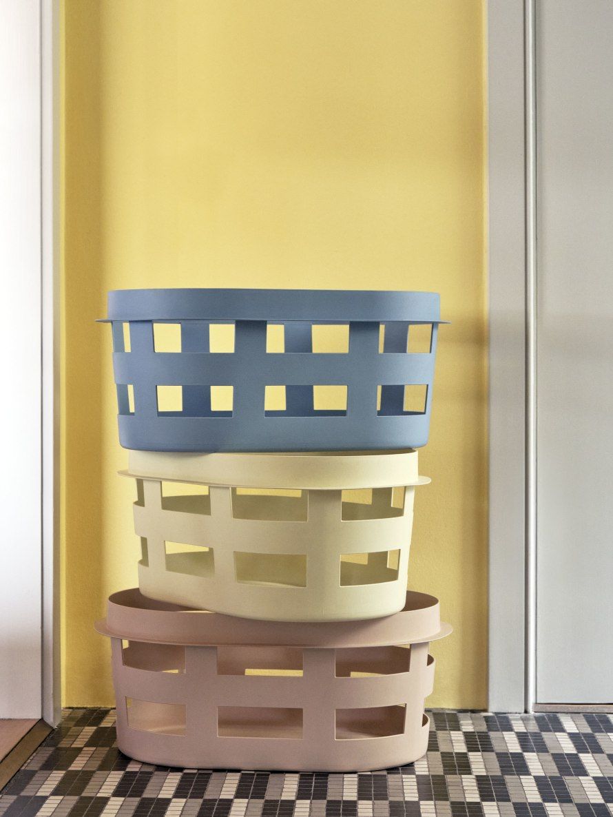 Gestapelte Hay Laundry Basket Wäschekörbe in Blau, Beige und Rosa vor gelber Wand.