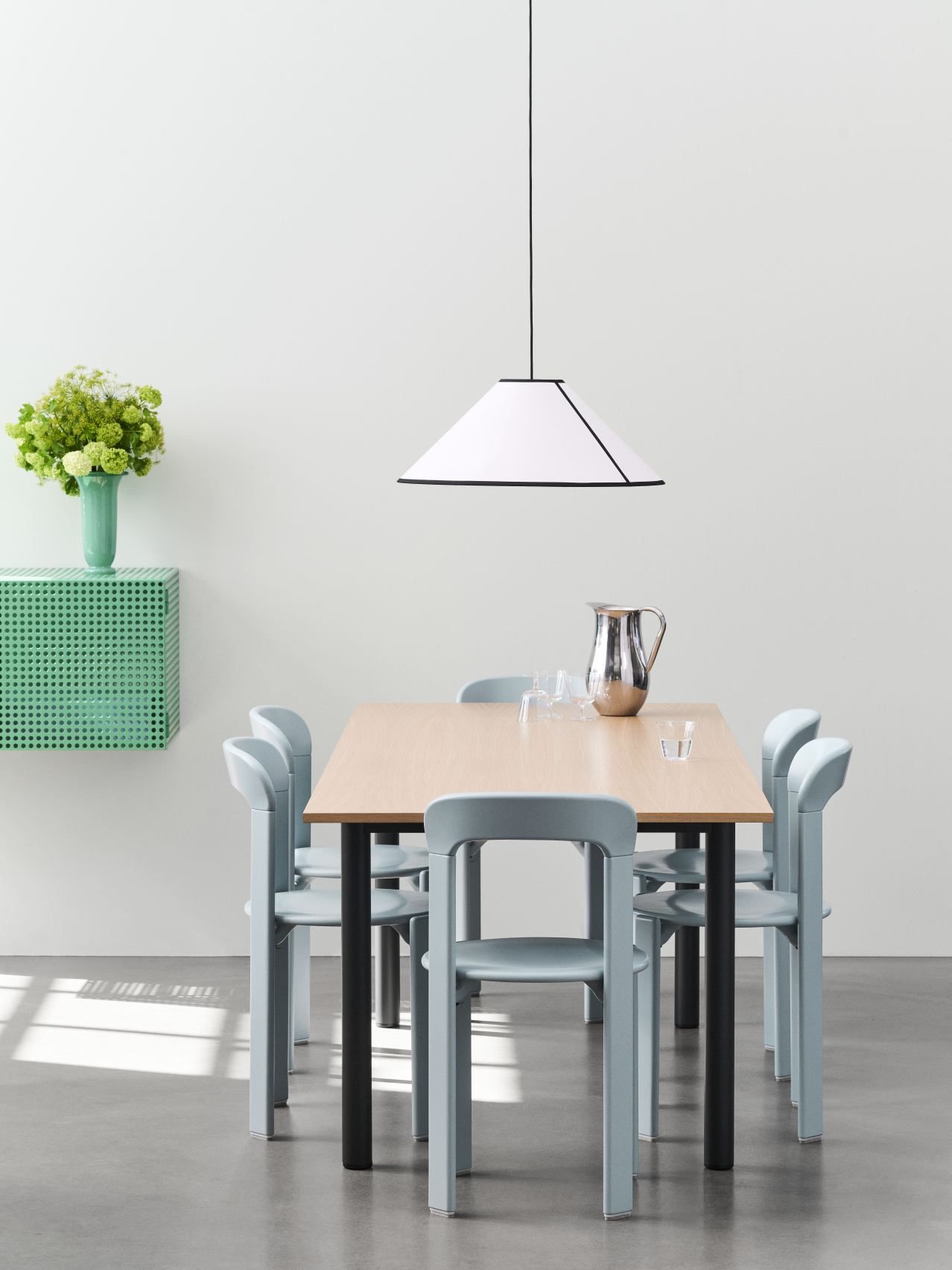 Helles Esszimmer mit Holztisch, blauen Stühlen und grünem Hay Perforated Cabinet Wall Sideboard an der Wand.