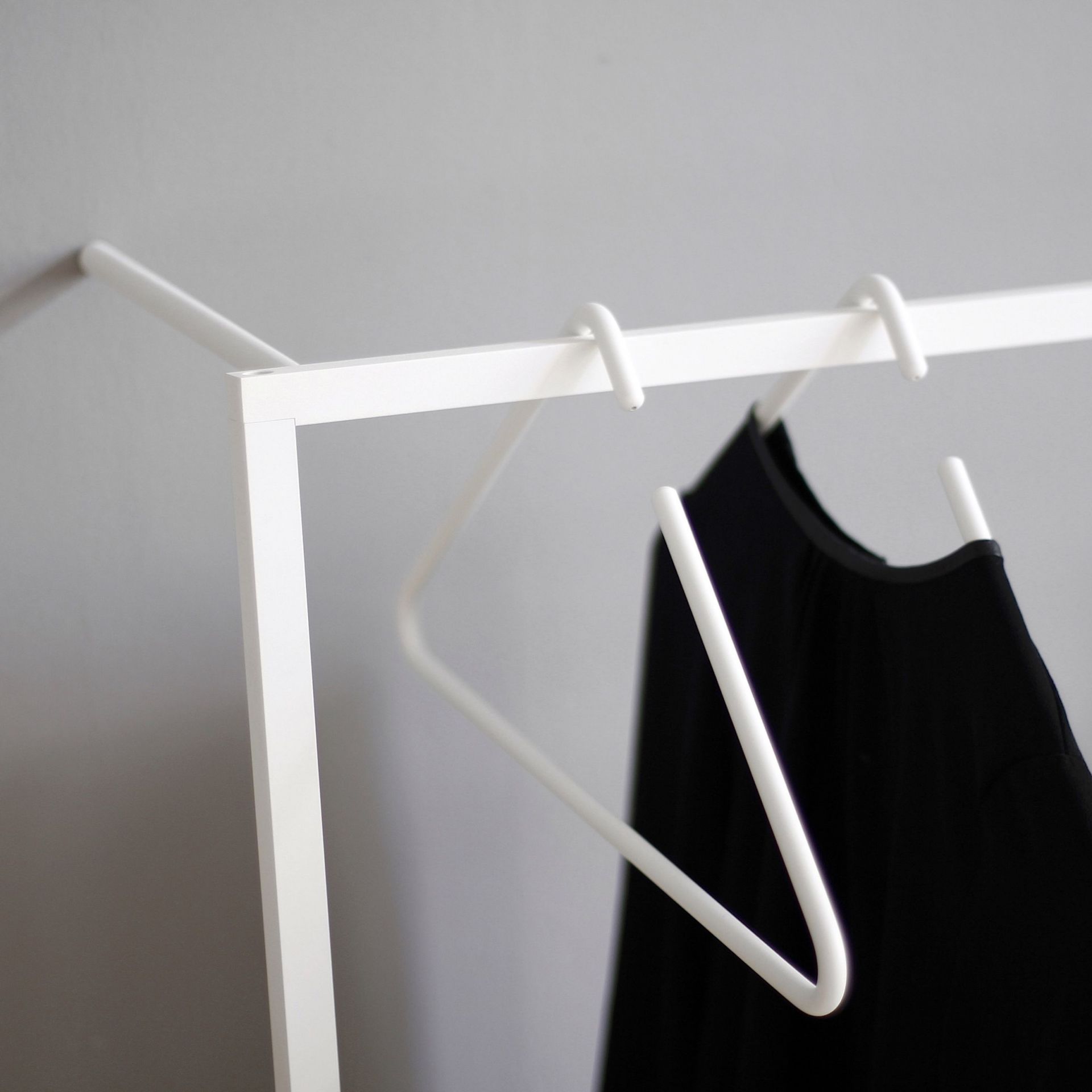 Detailaufnahme der weißen Leano Anlehngarderobe von Roomsafari mit Kleiderbügel und schwarzem Kleid.