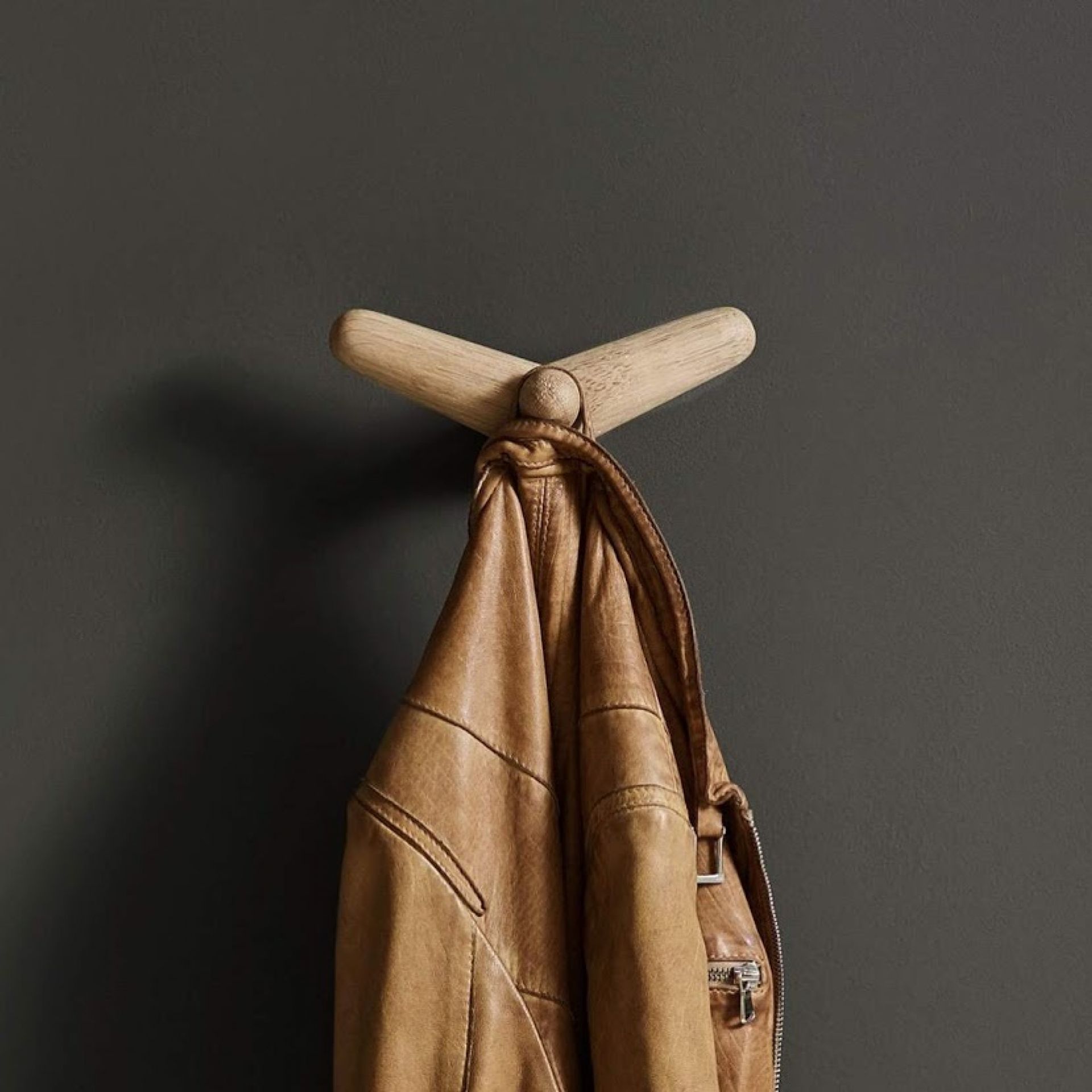 Tail Wing Haken von Woud, ein minimalistischer Garderobenhaken aus hellem Holz mit brauner Lederjacke.