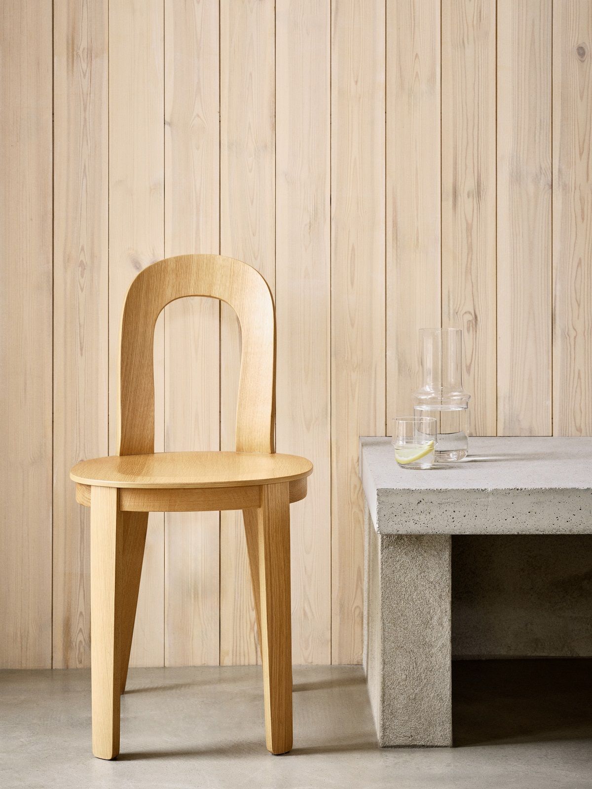 Olivia Chair von Design House Stockholm, heller Holzstuhl vor Holzwand, minimalistisches Design.