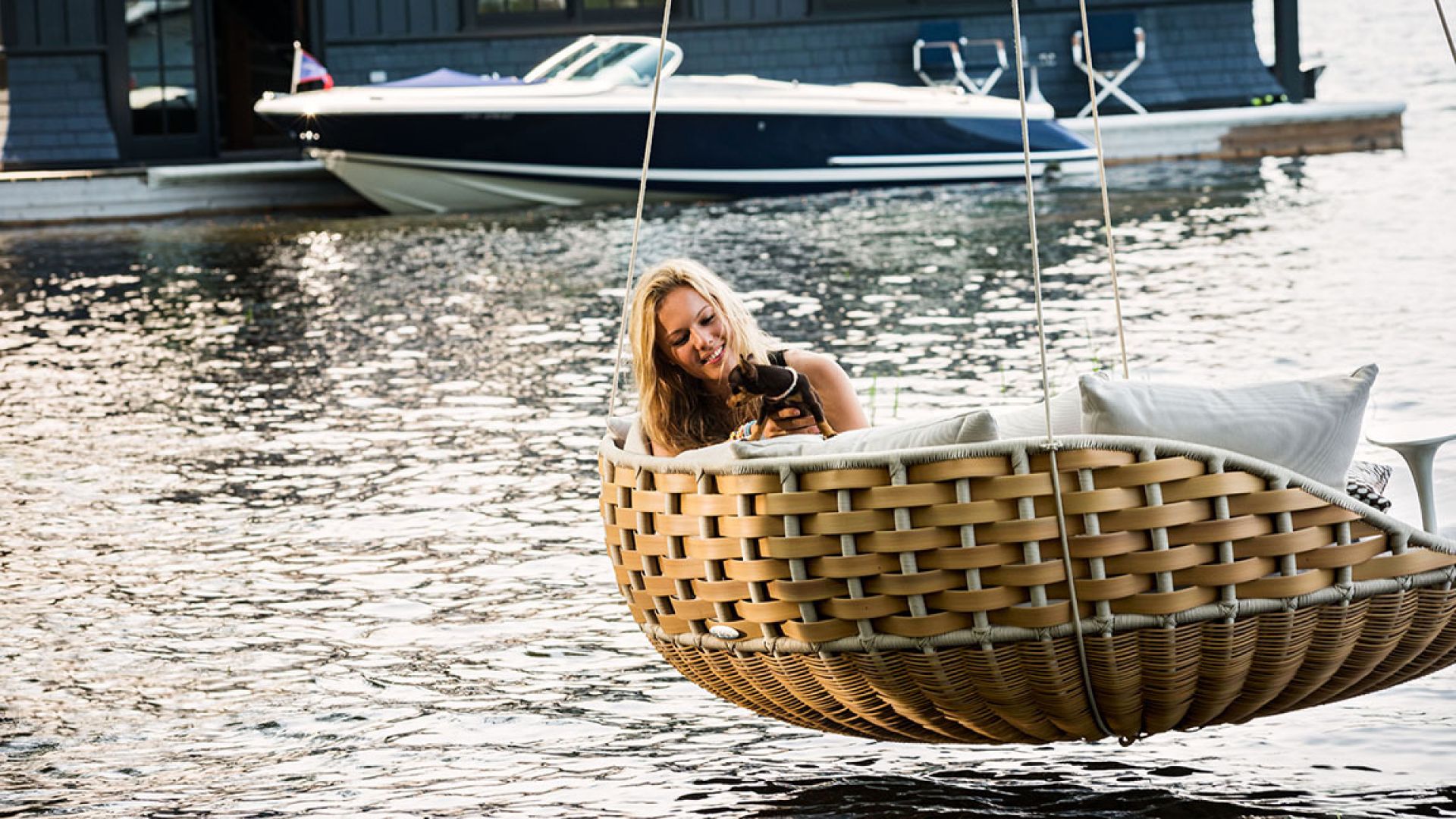 Frau entspannt mit Hund im Dedon Swingrest Hanging Lounger Hängesessel mit bequemen Sitzkissen über dem Wasser.