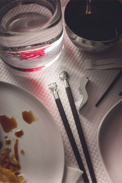 Alessi Anna Stick Essstäbchen Set auf gedecktem Tisch mit Geschirr und Glückskeks.