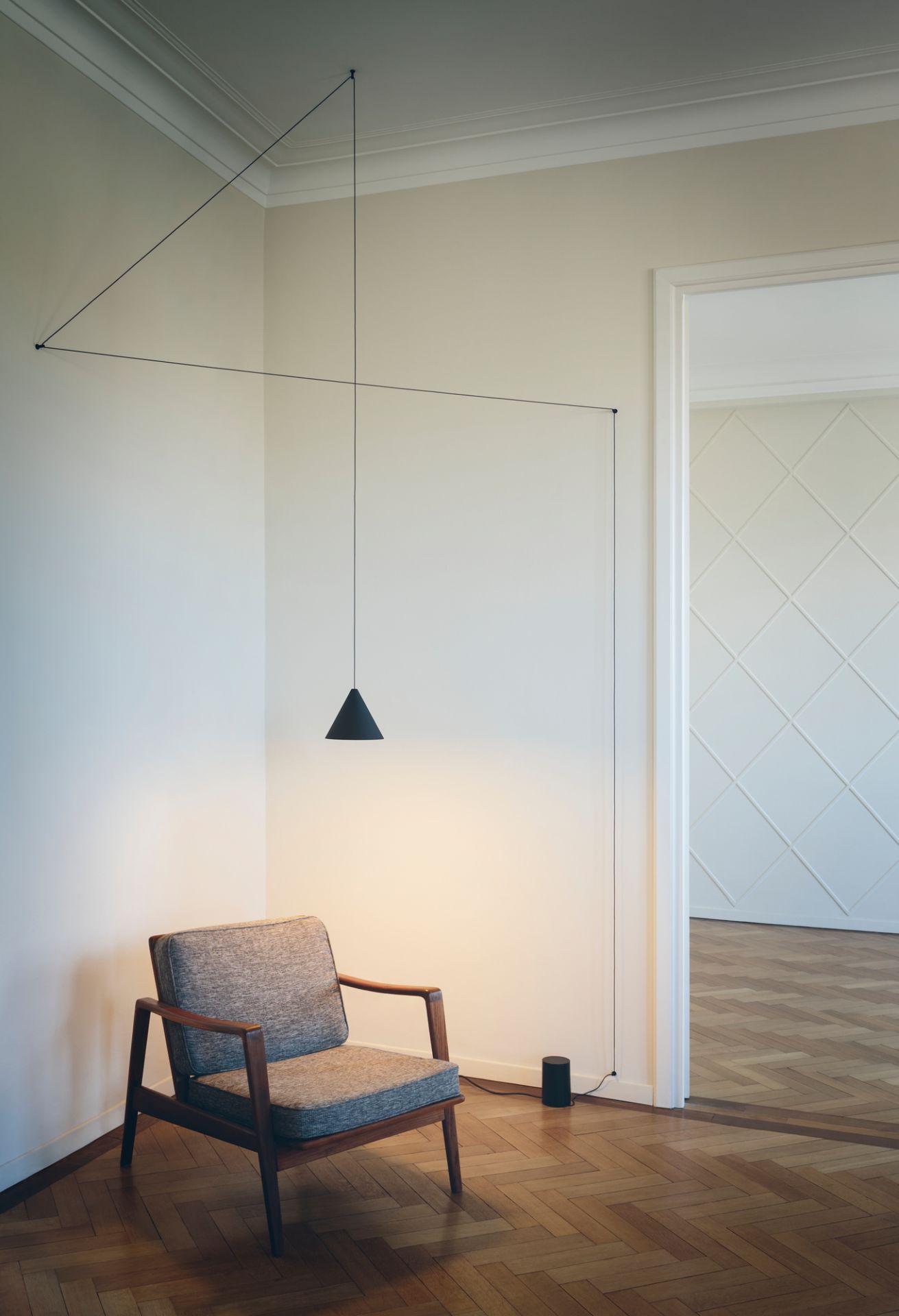 Flos String Light Cone Pendelleuchte über Sessel in modernem Wohnzimmer mit Fischgrätparkett.
