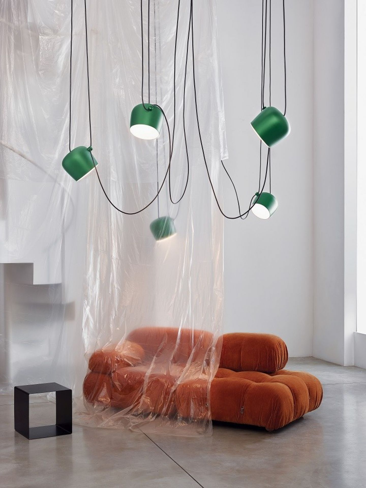 Grüne Aim Pendelleuchte von Flos über orangefarbenem Sofa mit schwarzem Beistelltisch in modernem Interieur.
