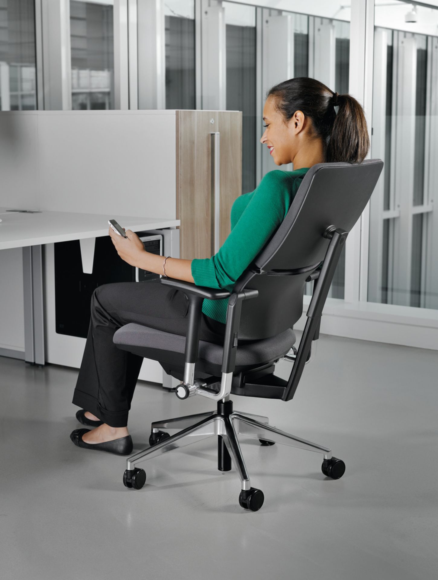 Frau sitzt auf einem grauen Please Drehstuhl von Steelcase und bedient ihr Smartphone.