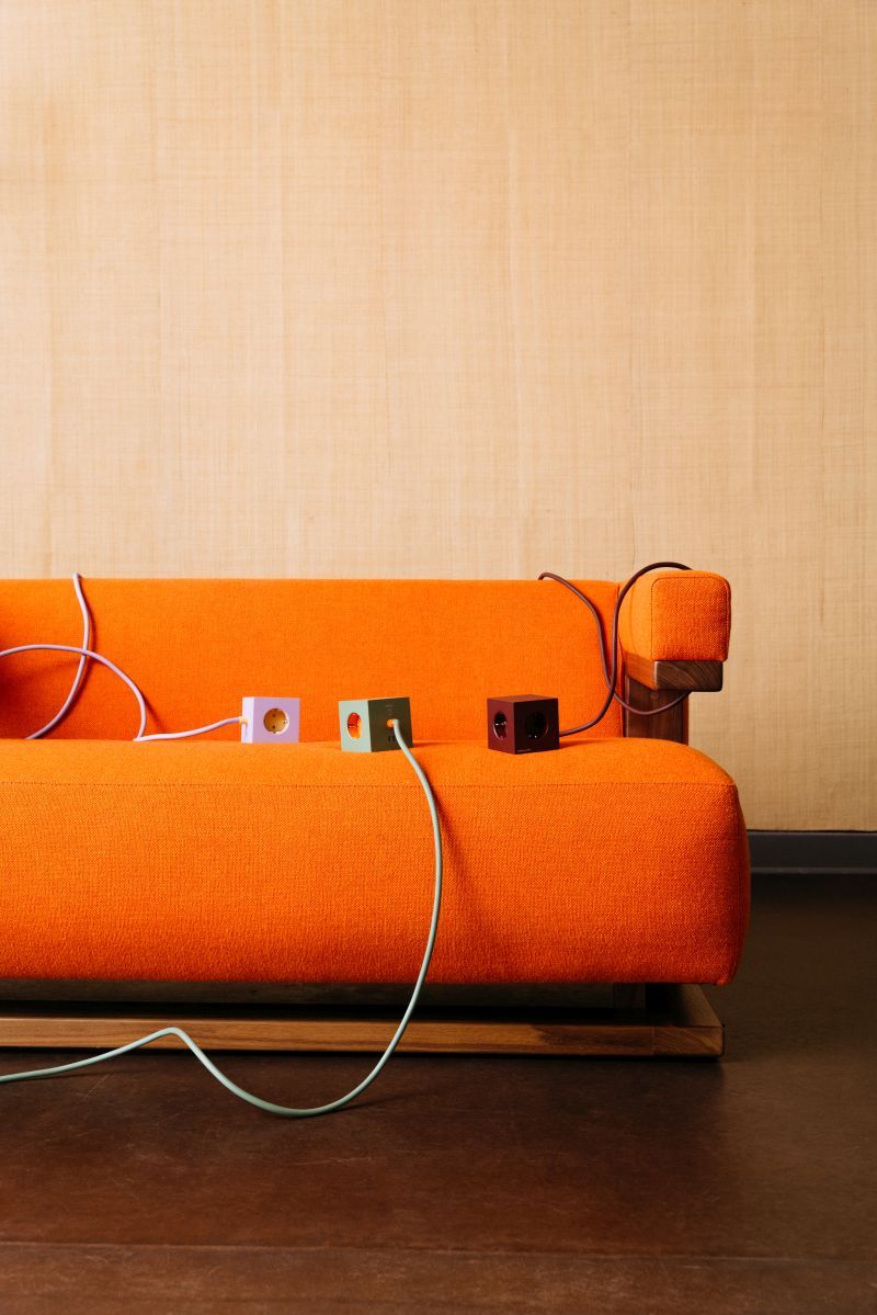 Avolt Square 1 Bauhaus Edition Steckdosenwürfel in Lila, Grün und Schwarz auf orangefarbenem Sofa.