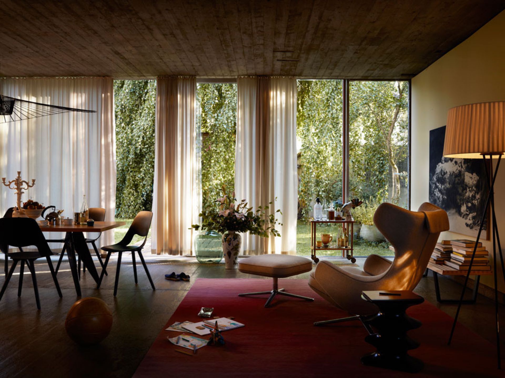 Heller Wohnraum mit Vitra Grand Repos Sessel und Hocker auf rotem Teppich vor Fensterfront.