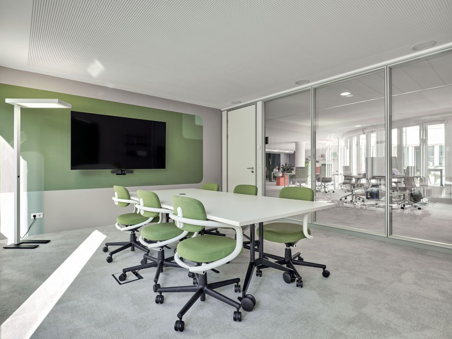 Besprechungsraum mit Vitra MedaMorph Klapptisch, weißen Tischplatte, grünen Stühlen und großem Bildschirm an der Wand.