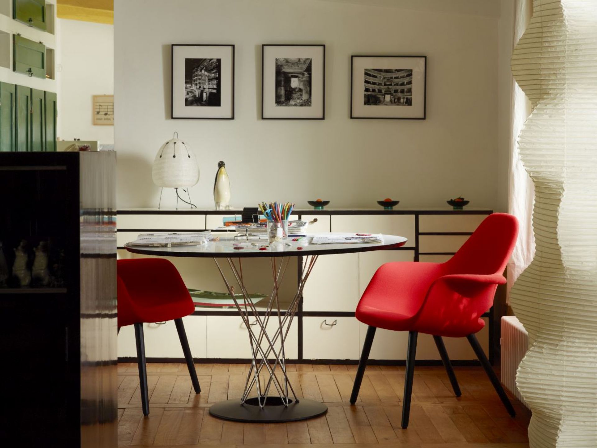 Noguchi Dining Table von Vitra mit Glasplatte und verchromtem Drahtgestell, umgeben von roten Stühlen.