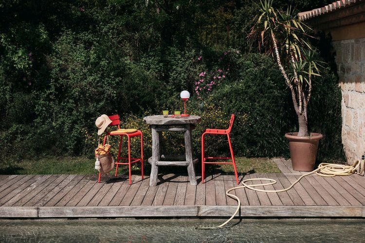 Roter Fermob Luxembourg Barhocker Outdoor mit Tisch und Dekoration auf einer Holzterrasse am Pool.