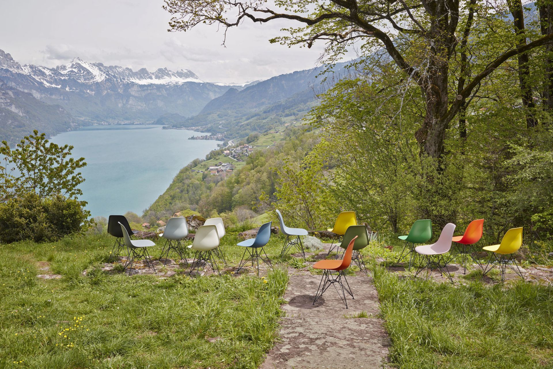 Eine Gruppe von Eames Plastic Arm Chairs DAR Stühlen von Vitra in verschiedenen Farben vor Bergpanorama.