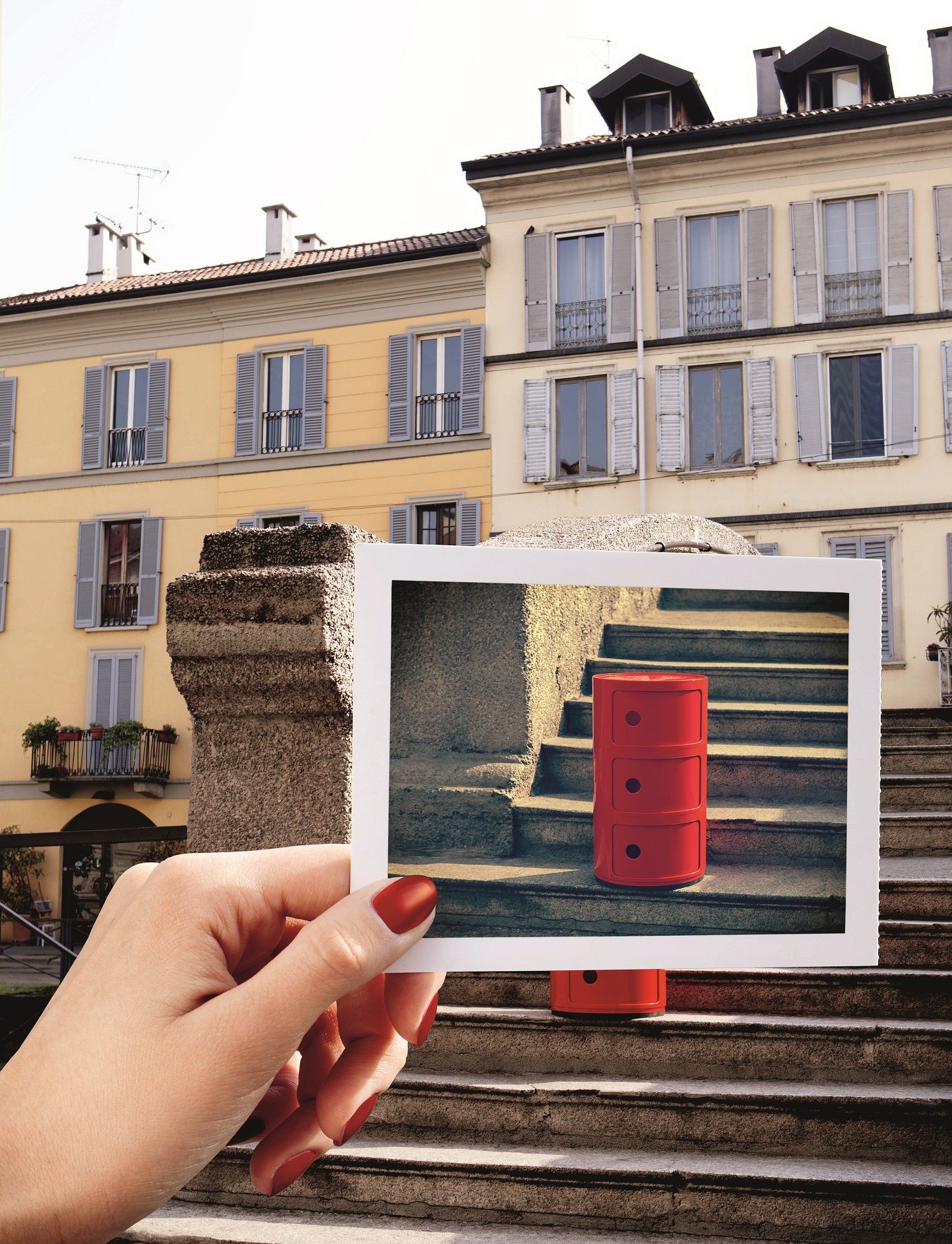 Roter Kartell Componibili Container mit drei Elementen auf einem Foto, gehalten vor italienischer Architektur.