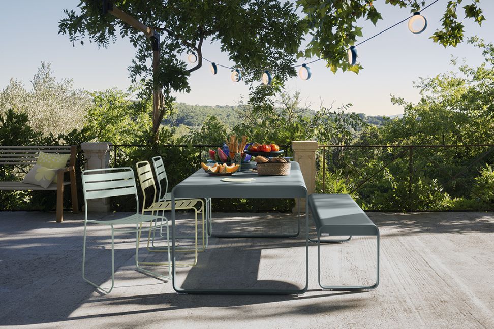 Bellevie Tisch von Fermob im Outdoor-Bereich mit Stühlen und Bank, ideal für Garten und Terrasse.