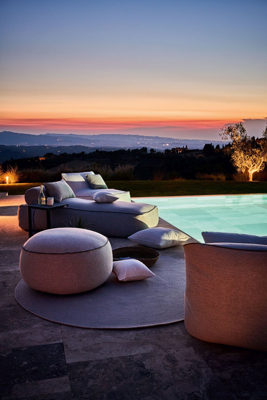 Maliha Lounge Sessel von Weishäupl Outdoor mit Hocker und Kissen am Pool bei Sonnenuntergang.