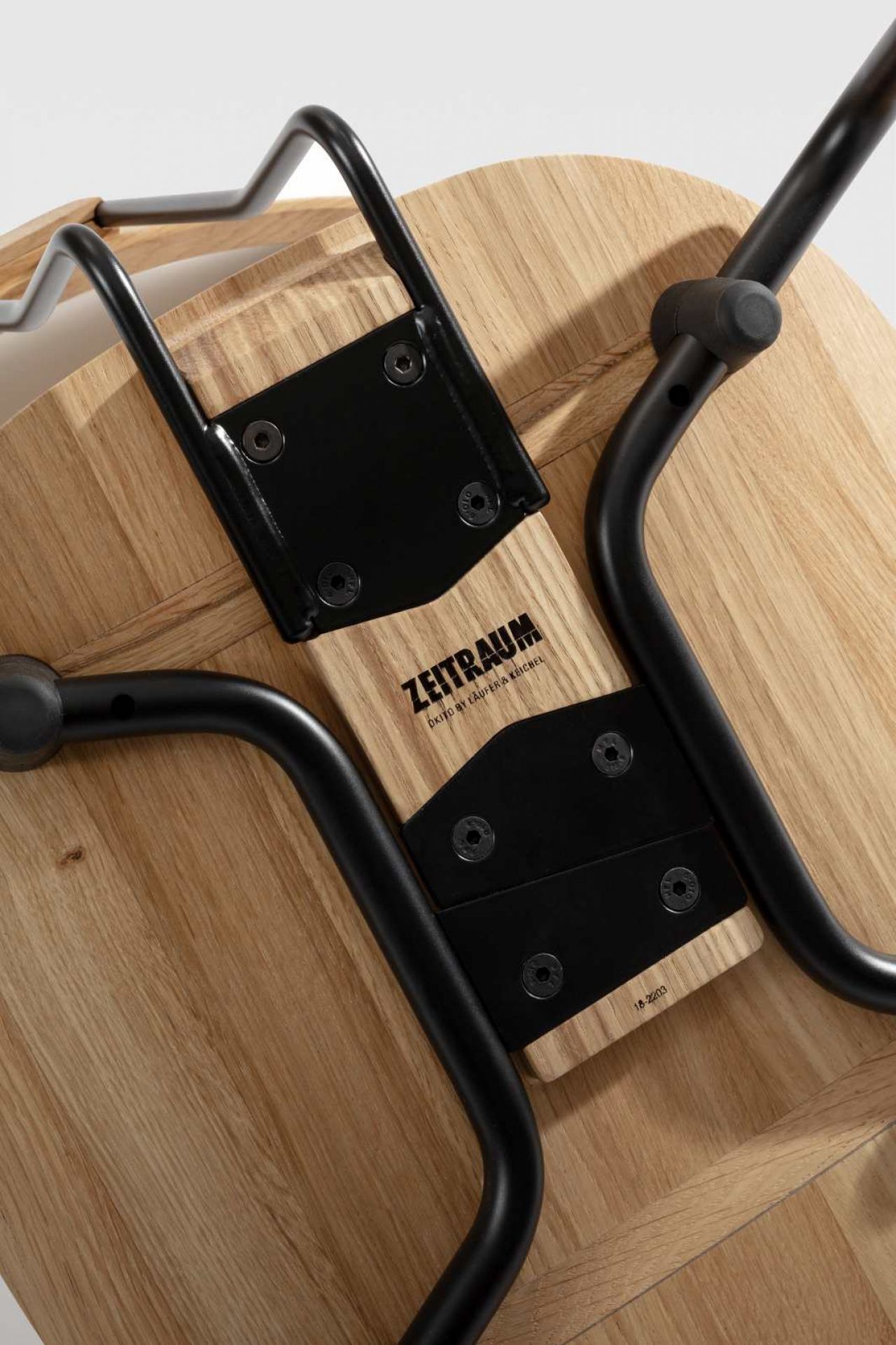 Detailaufnahme der Unterseite des Okito Stuhls von Zeitraum mit schwarzem Metallgestell und Holzstruktur.